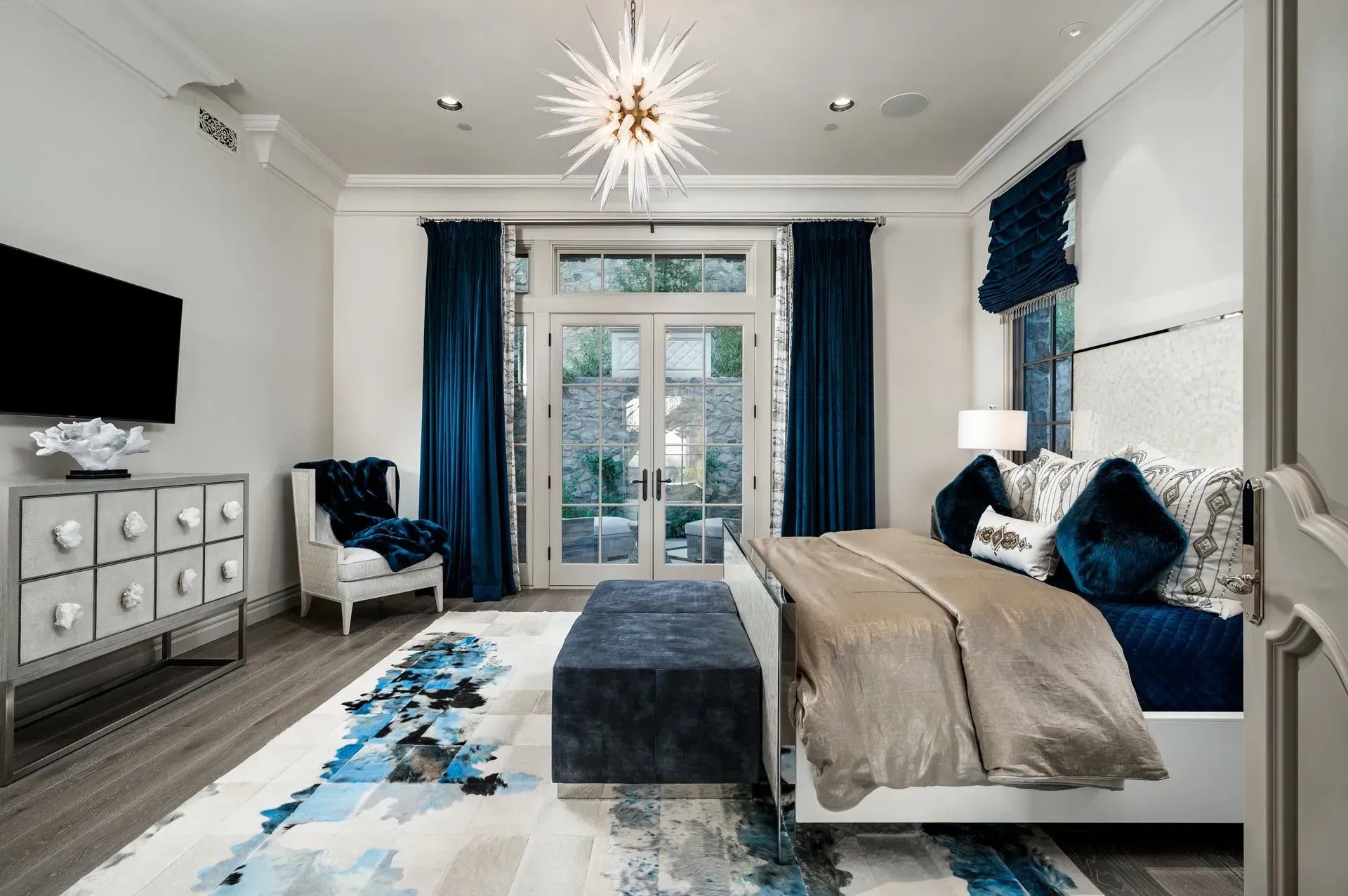 Luxurious bedroom with blue accents, bed, chest, chair, and access to a garden.