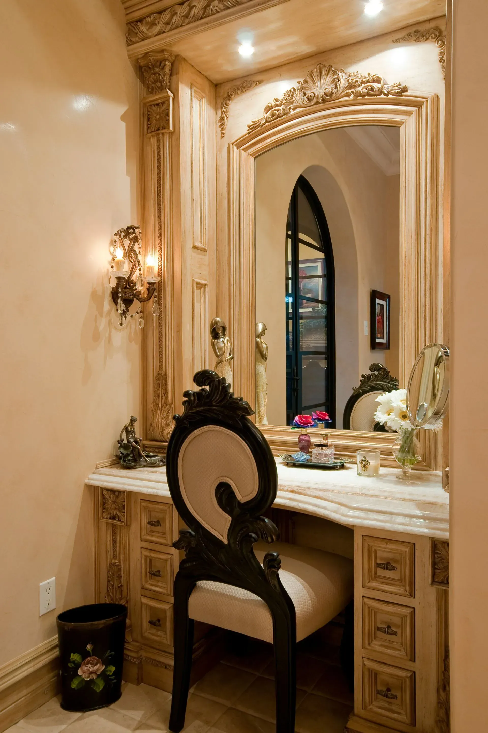 Vanity area with ornate carved wood, marble countertop, large mirror, and decorative chair.