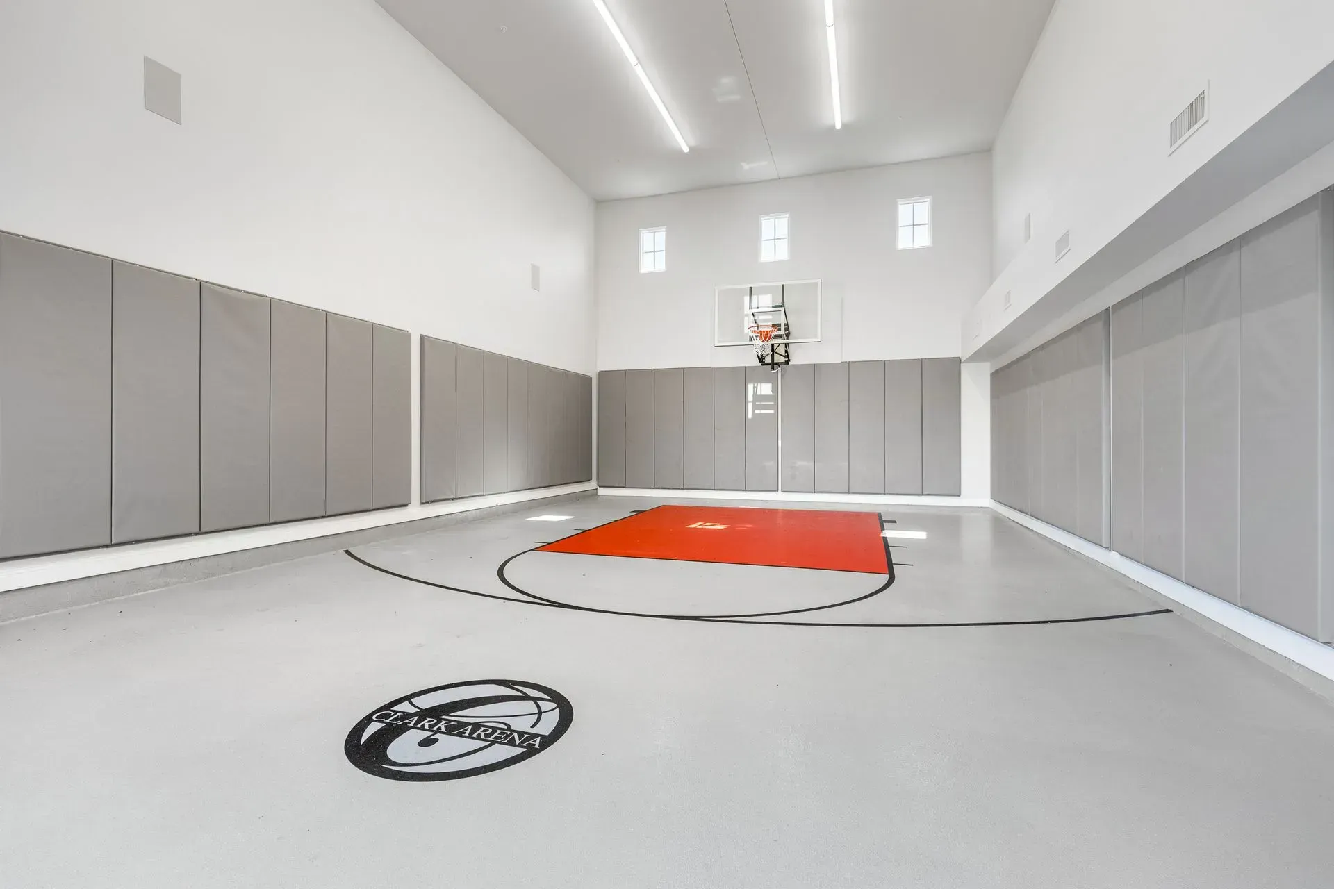 Indoor basketball court with red/orange key, gray floor, white walls, and padding.