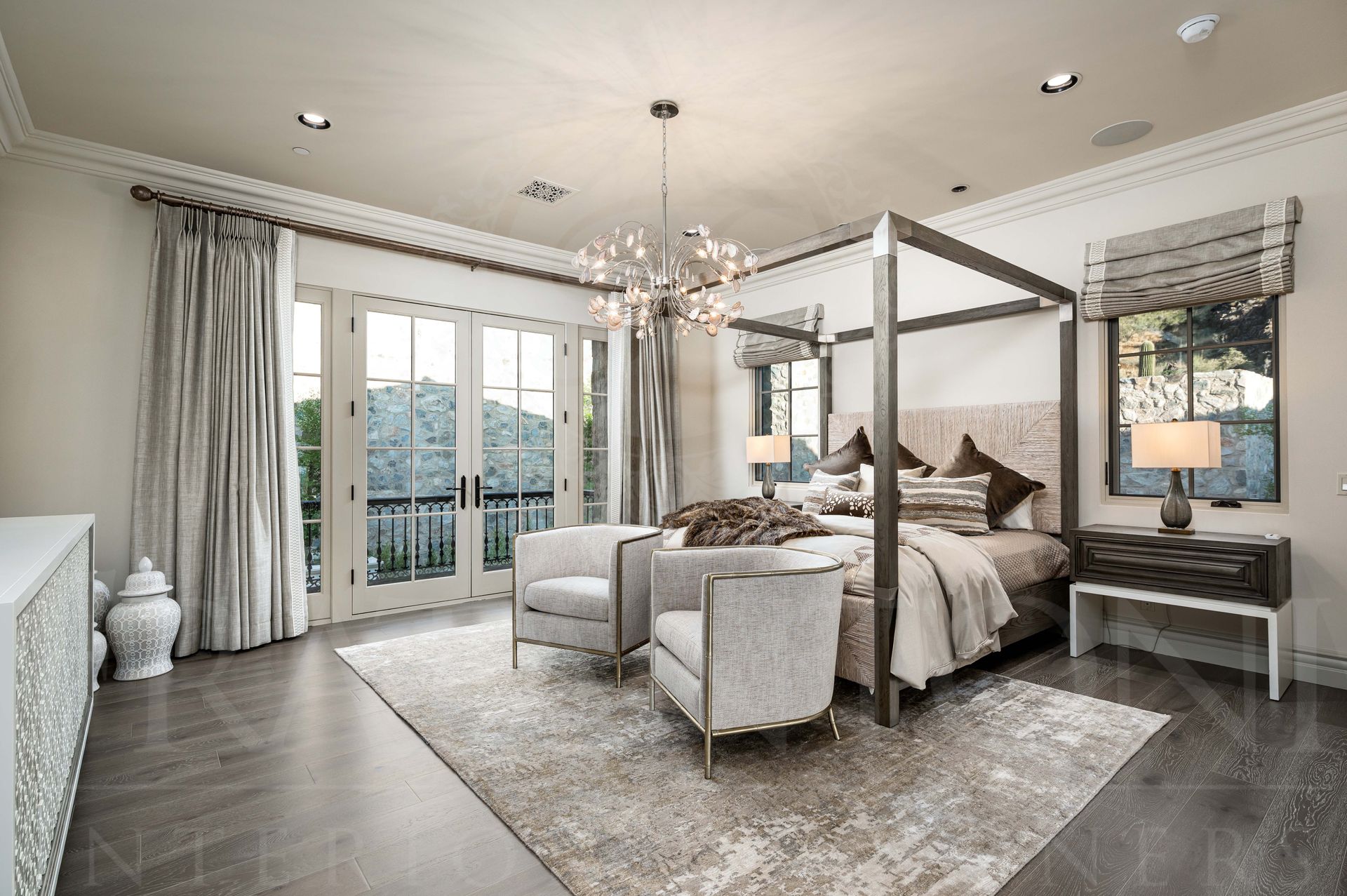 Elegant bedroom with canopy bed, soft gray decor, a statement chandelier, seating, large windows, and balcony doors which showcase desert mountain views