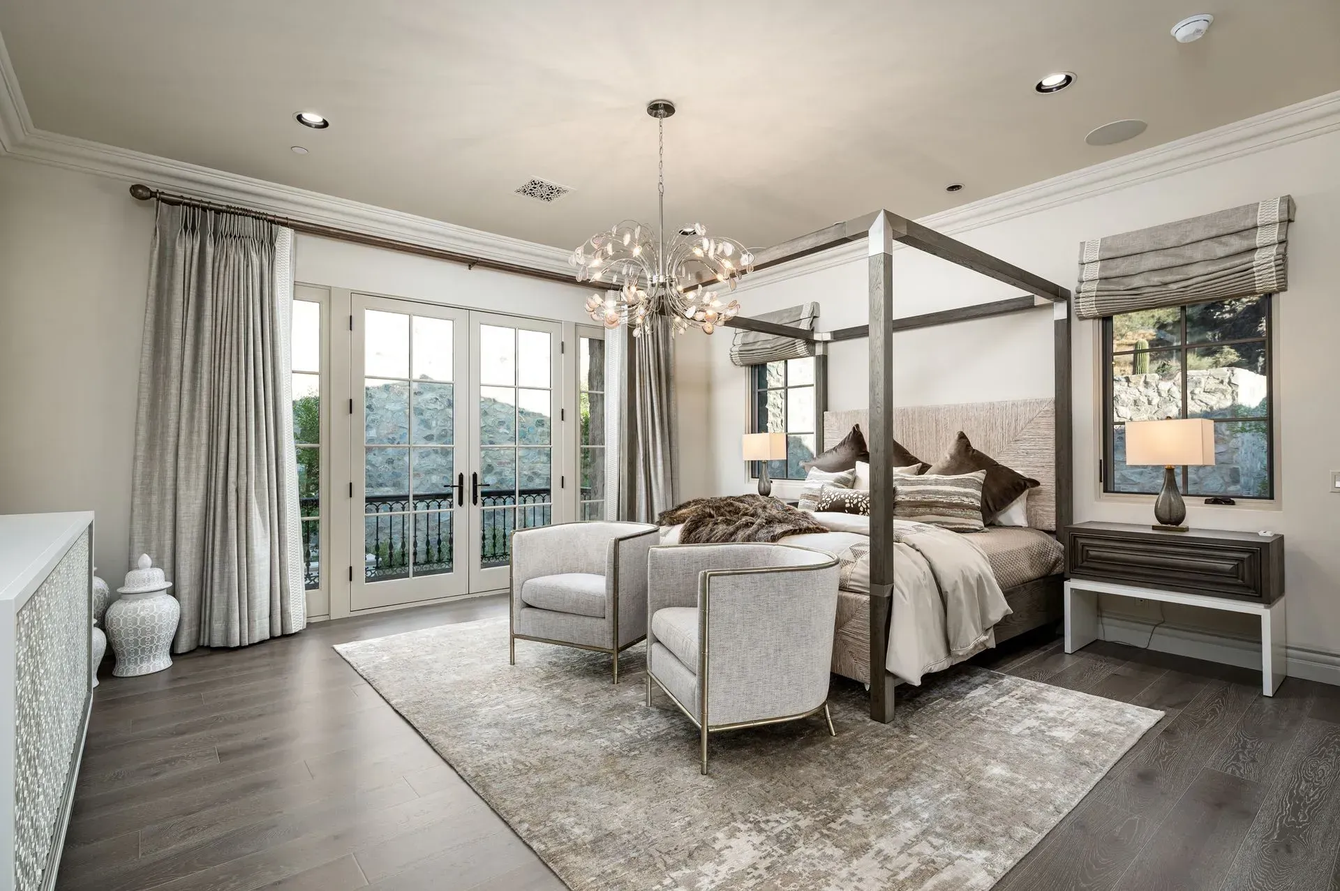 Luxury bedroom with a four-poster bed, two armchairs, and a balcony view.
