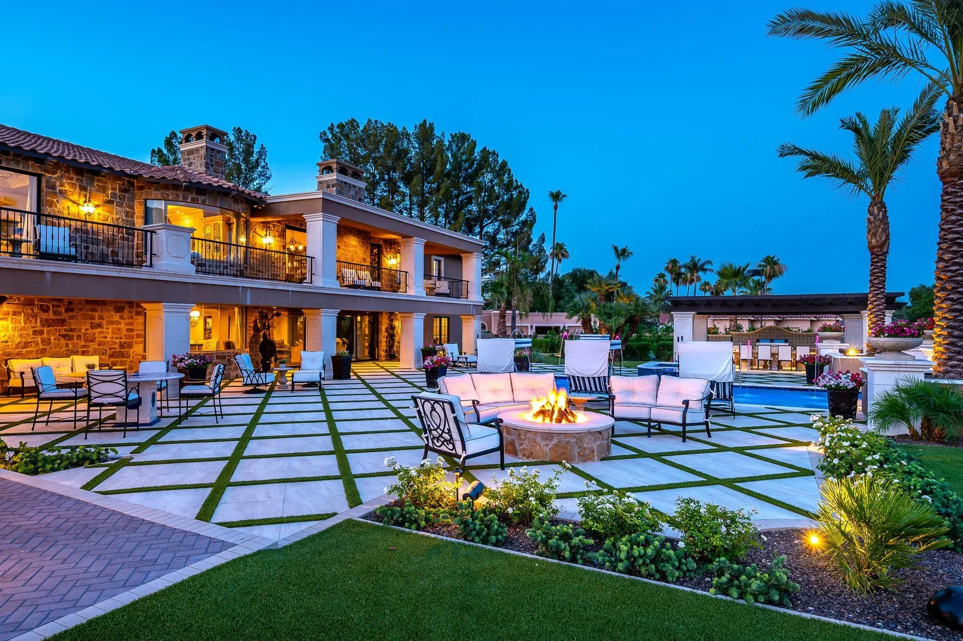 Luxury outdoor patio with seating, fire pit, and pool at dusk.