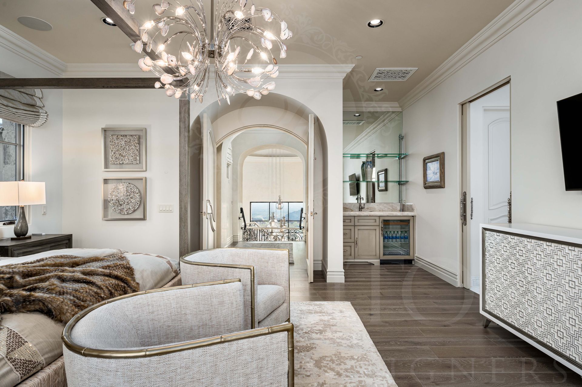 Luxury bedroom with four-poster bed, gray seating, large arched doors, a statement chandelier, and neutral decor