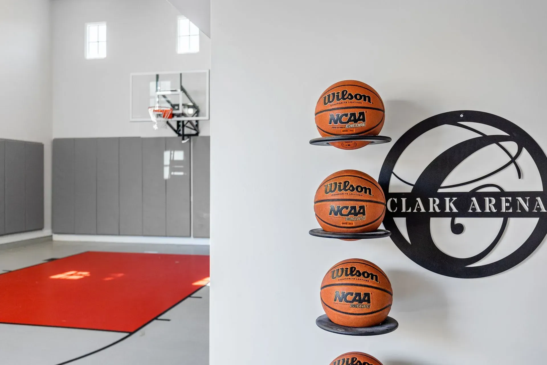 Basketball court with balls on shelves. A hoop and red mat are visible. 