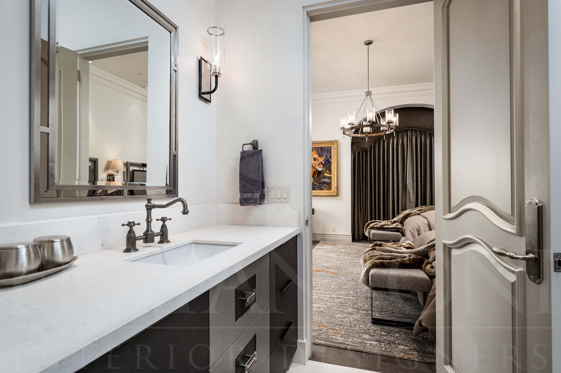 Elegant ensuite bathroom vanity with large mirror, white marble countertop, and open doorway to a carpeted guest bedroom.
