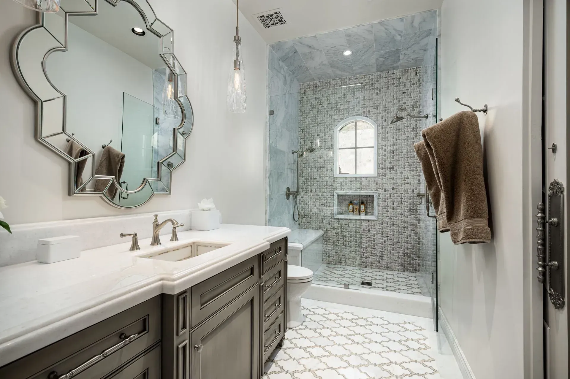 Elegant bathroom with marble accents, glass shower, ornate mirror, and gray vanity.