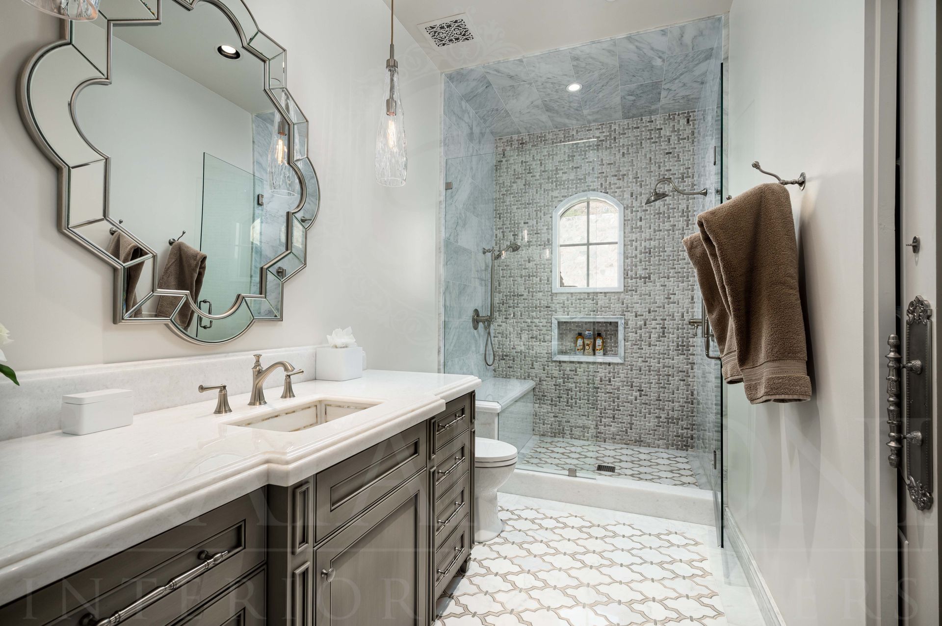 Bright custom bathroom with grey vanity, marble countertop, inlaid detailed sink, ornate mirror, glass shower with a shower bench, and white tile floor designed by Fratantoni Interior Designers in scottsdale, arizona