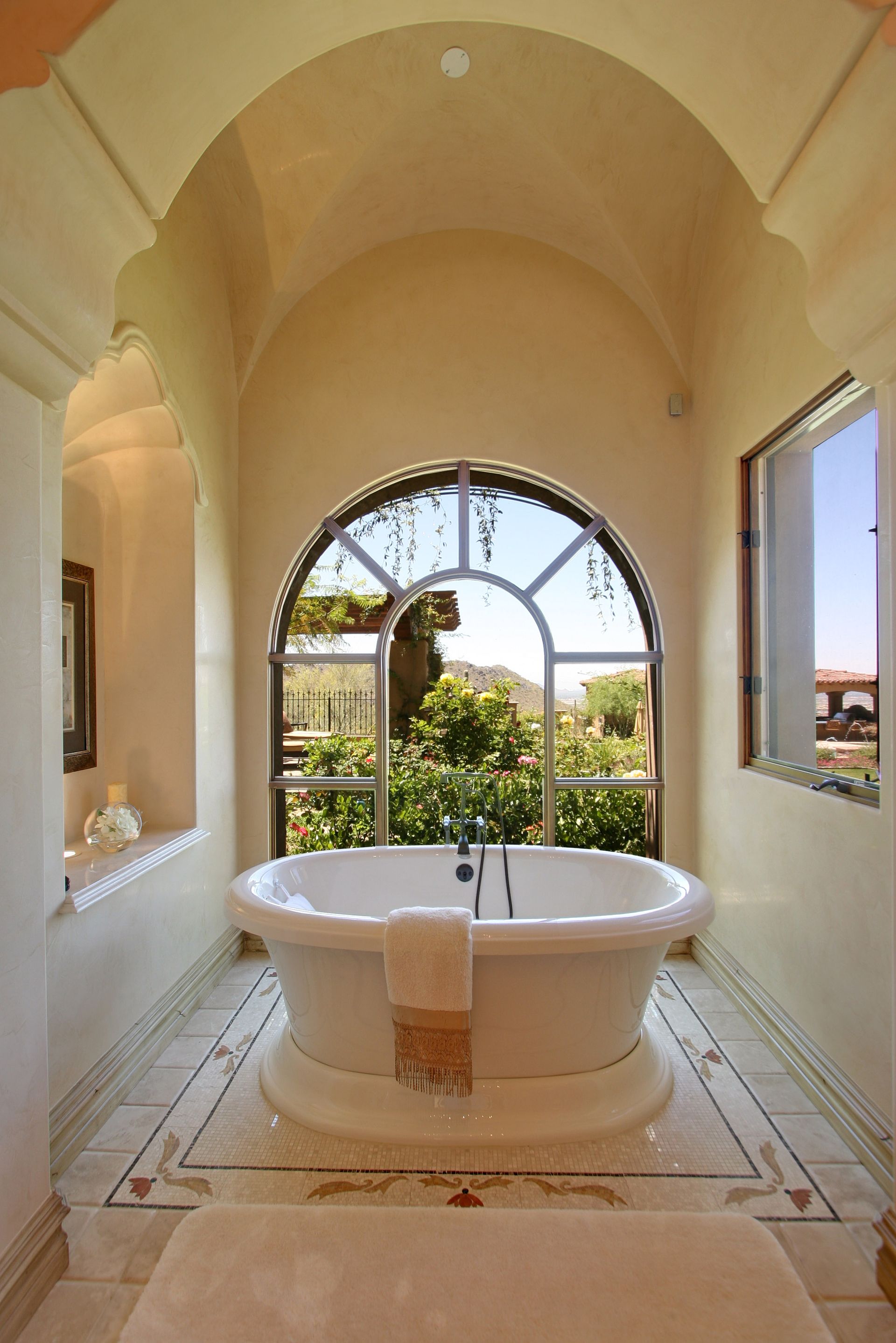 Elegant bathroom with arched window, freestanding tub, and marble tile floor.