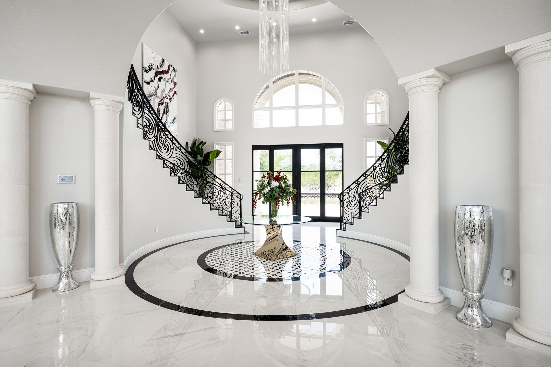 Grand luxury foyer with curved staircases, marble flooring, and symmetrical columns