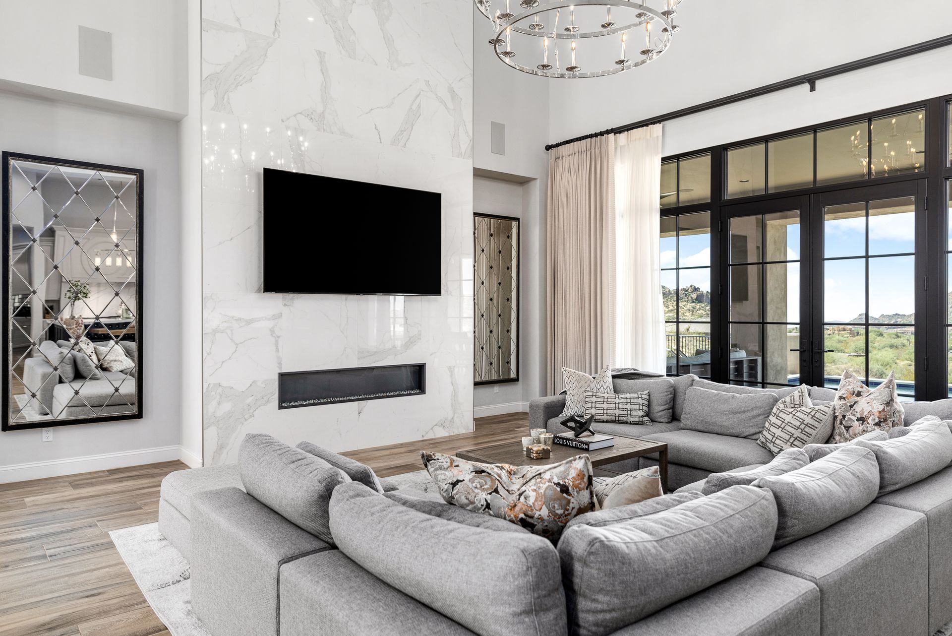 Living room with gray sectional sofa, fireplace, large TV, and tall windows.