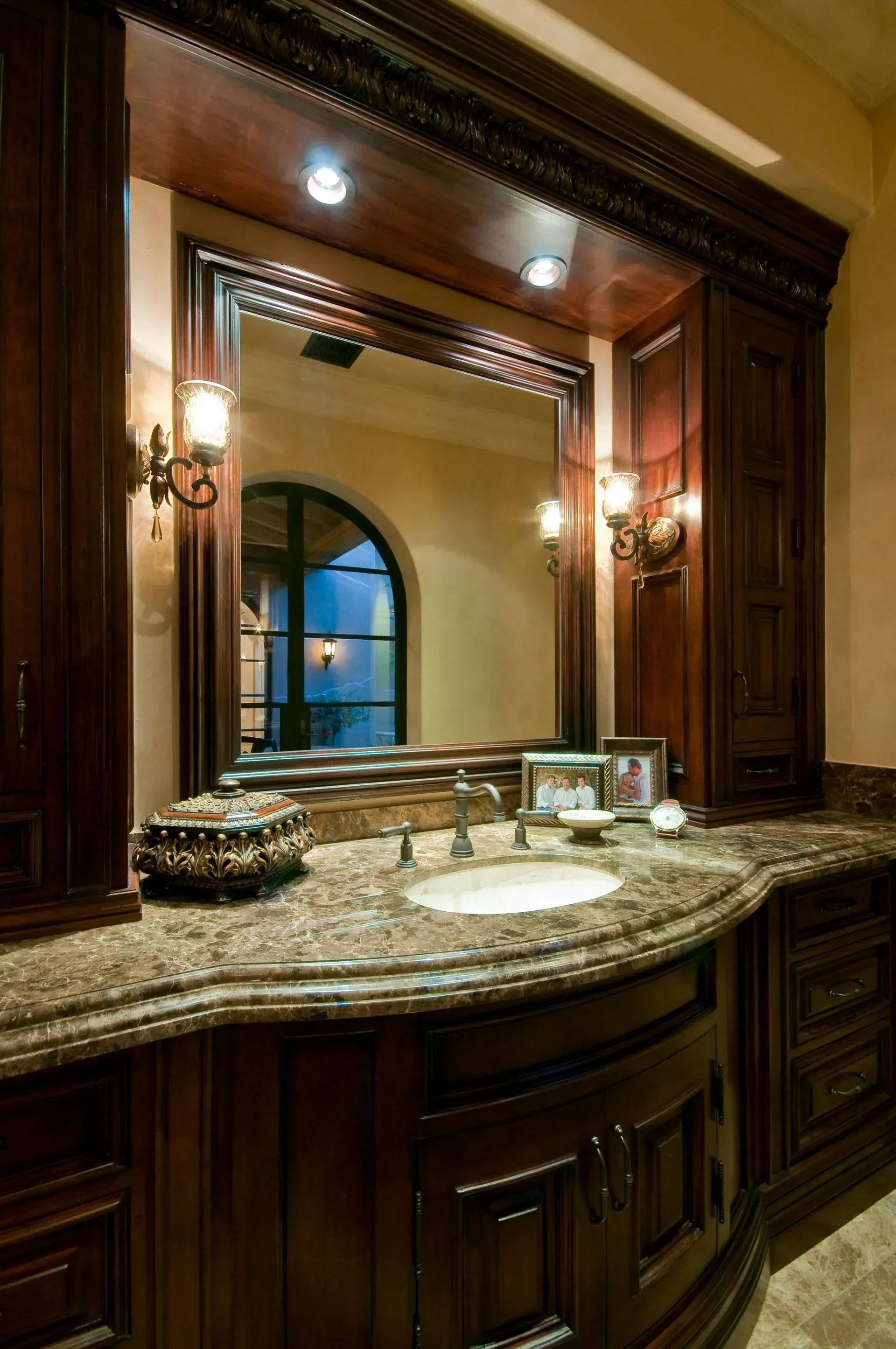 Dark wood vanity with granite countertop, large mirror, and sconces.