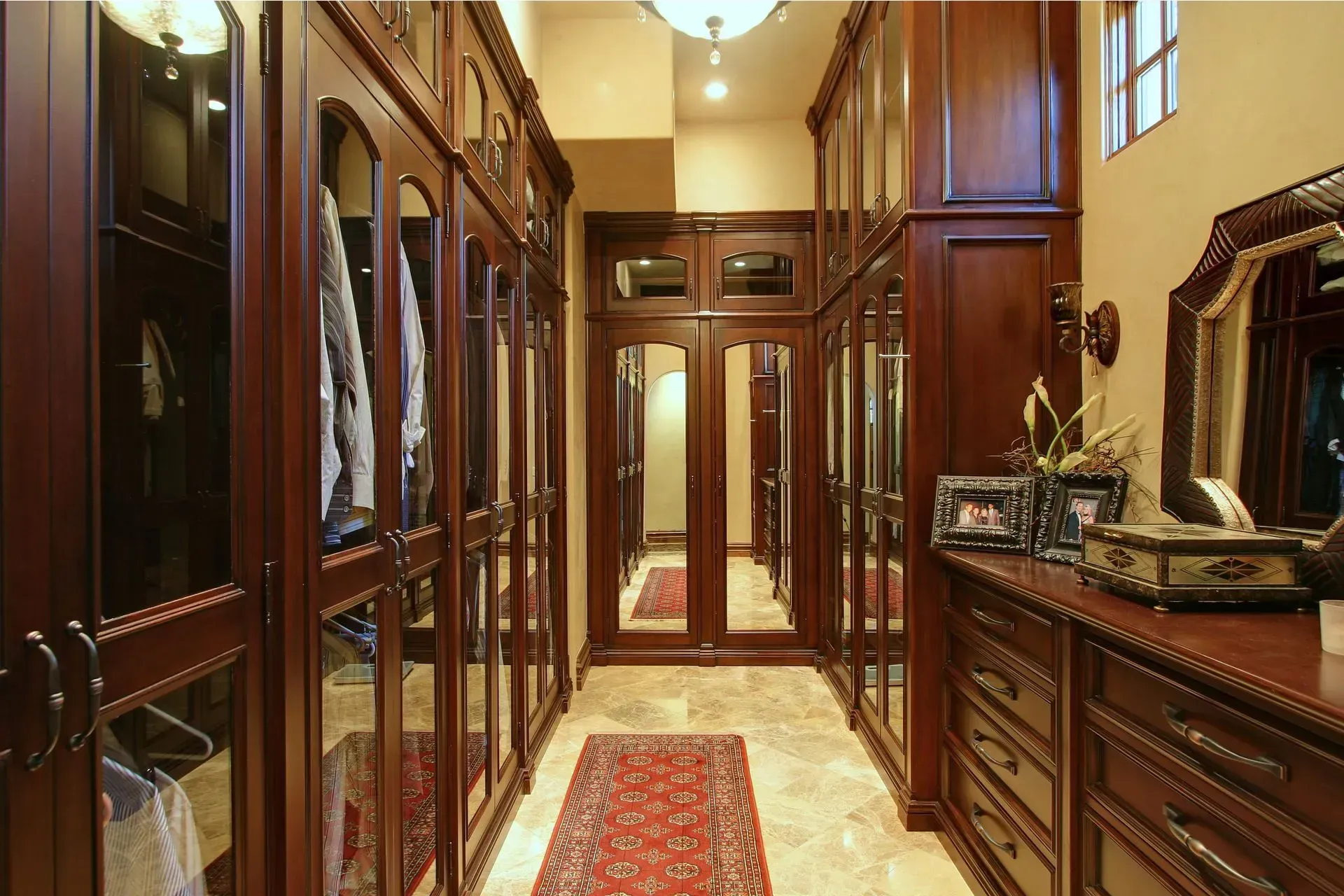 Walk-in closet with dark wood cabinets, glass doors, and a patterned rug on a stone floor.
