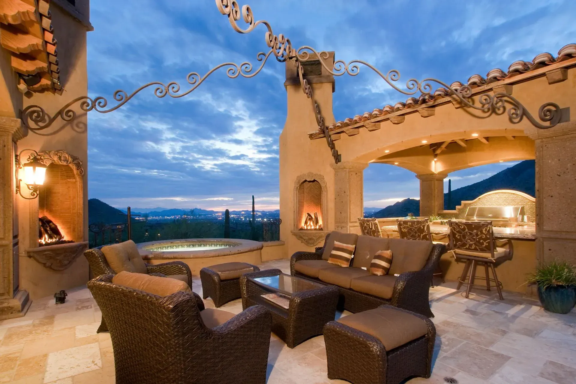 Outdoor patio with seating, fireplaces, and a grill, overlooking a scenic valley under a twilight sky.