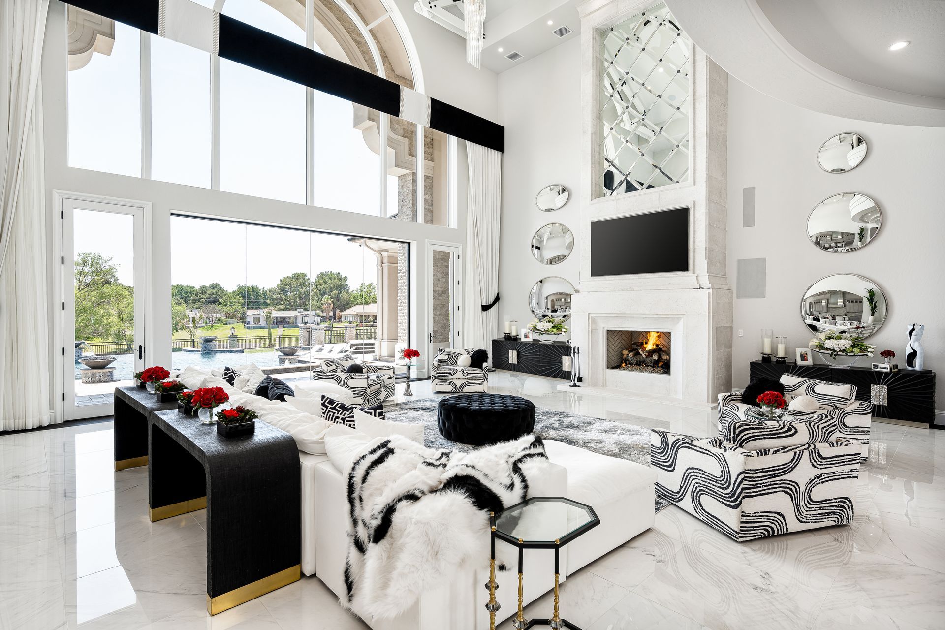 Luxurious living room with white and black decor, large windows, and fireplace.