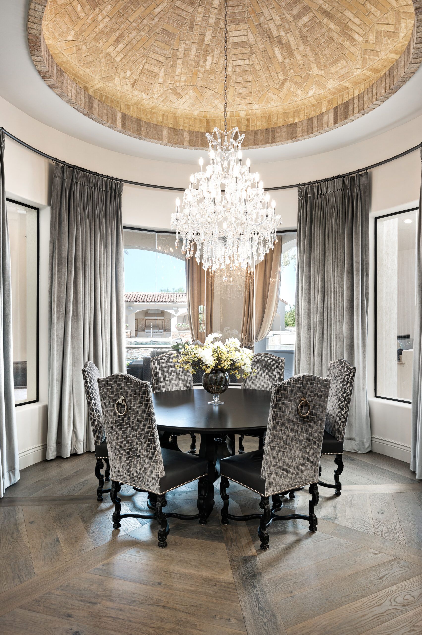 A dining room with a round table and chairs and a chandelier hanging from the ceiling.