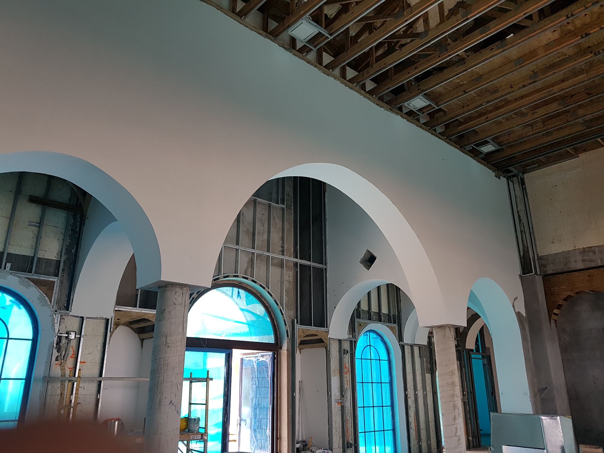 Interior of a building under construction, featuring arched windows and a painted ceiling.