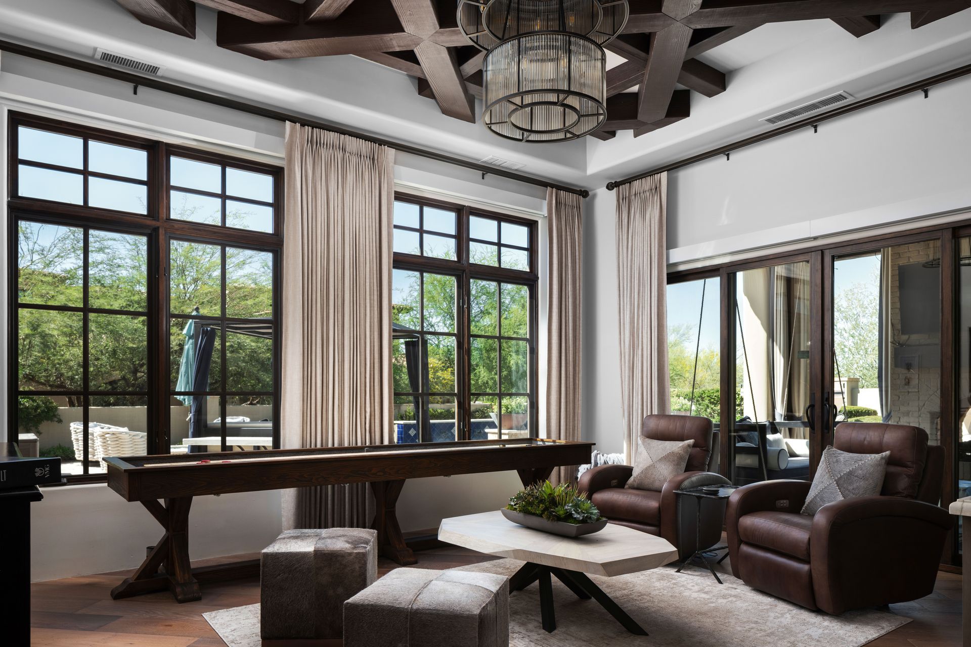 Living room with dark wood framed windows and ceiling beams, leather chairs, and a shuffleboard table.