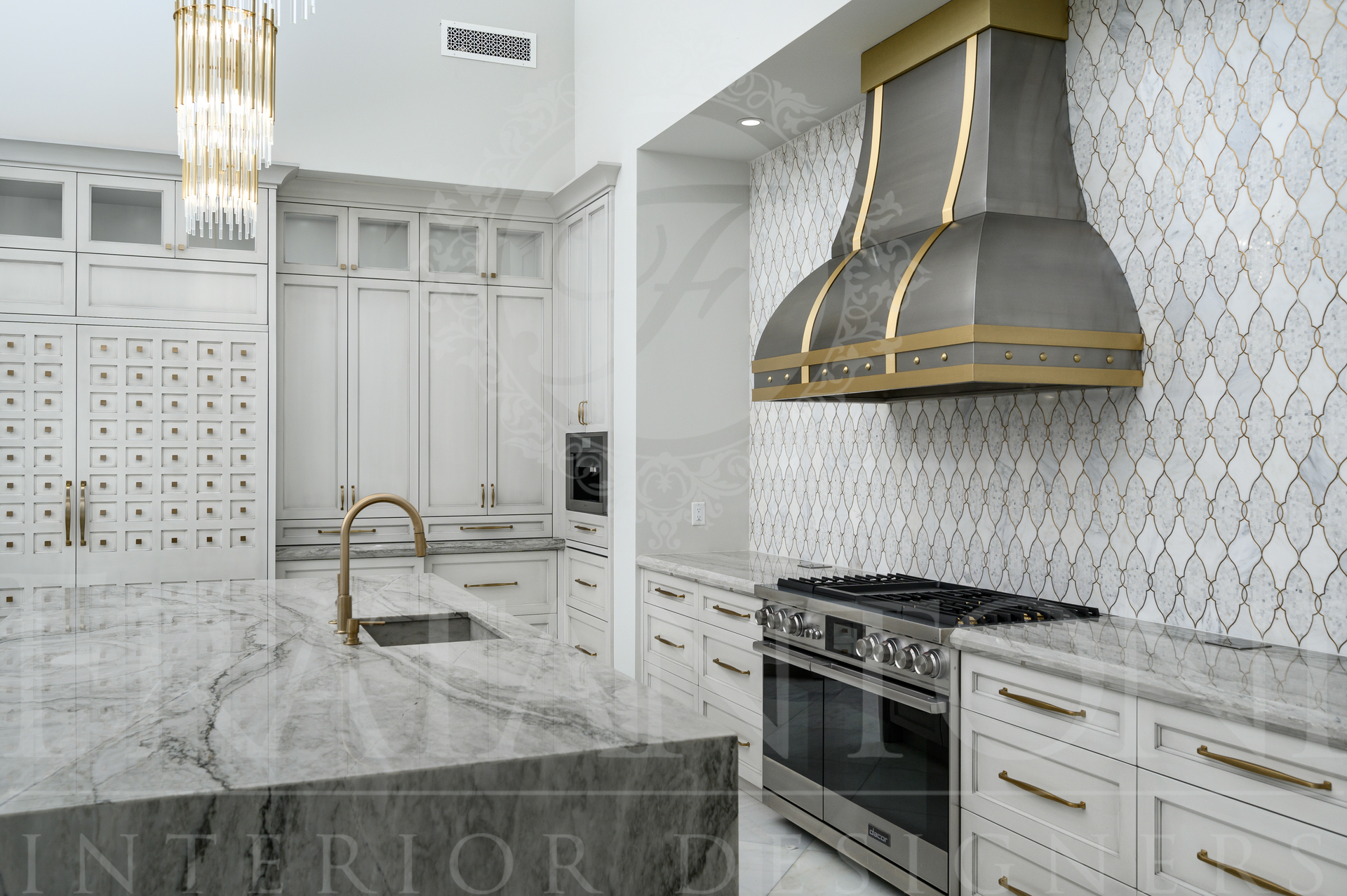 Elegant white kitchen with marble island, gold accents, and stove beneath a gold-trimmed custom range hood
