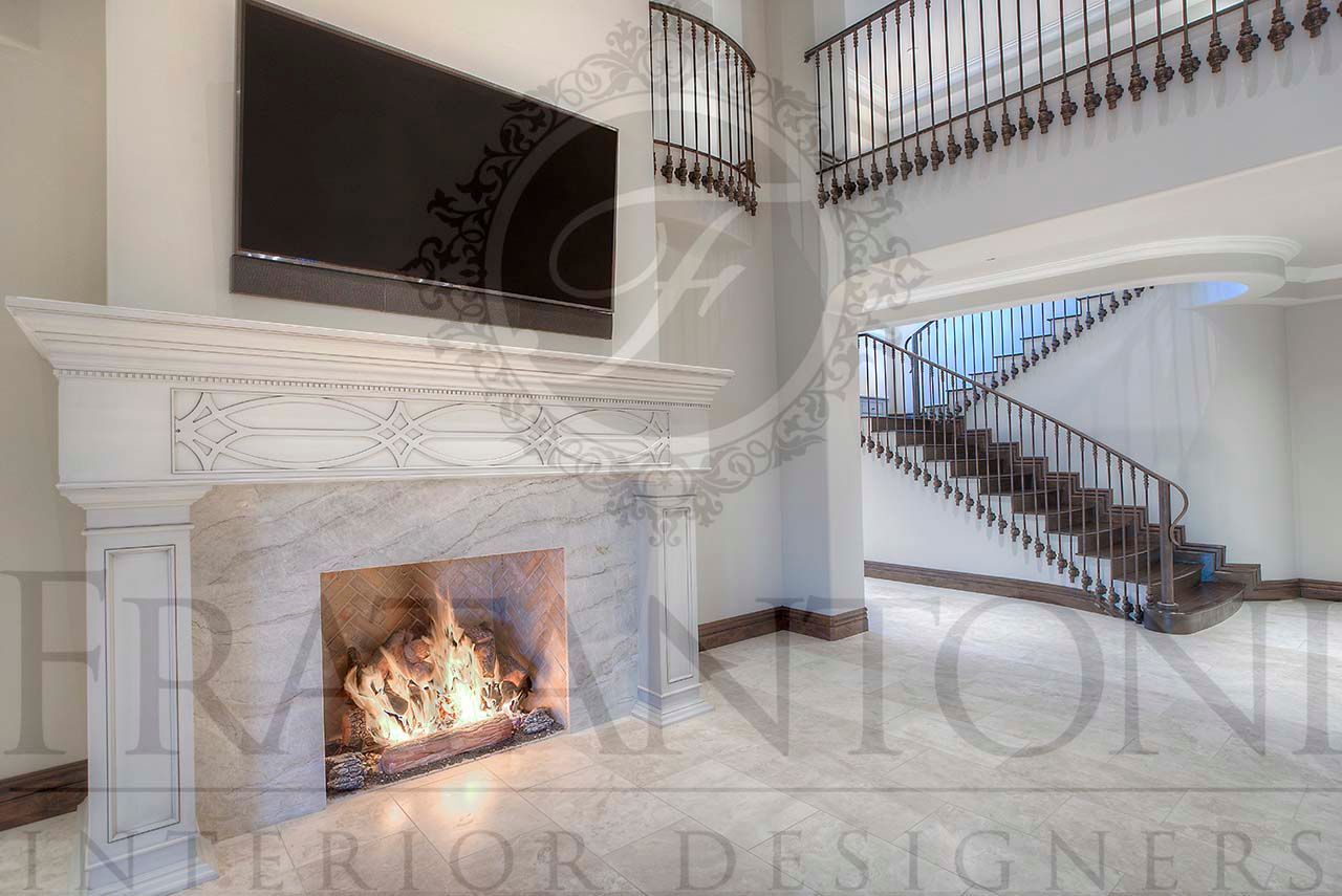 Luxurious living room with ornate fireplace, mounted TV, and curved staircase with wrought-iron railing on balcony