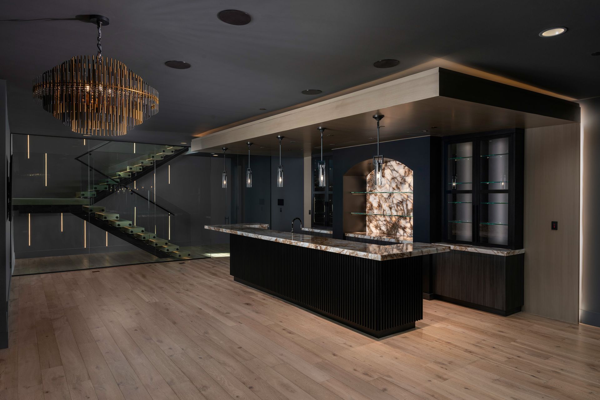 Dark bar area with a wooden floor, black bar, and stairs, accented by gold light fixtures.