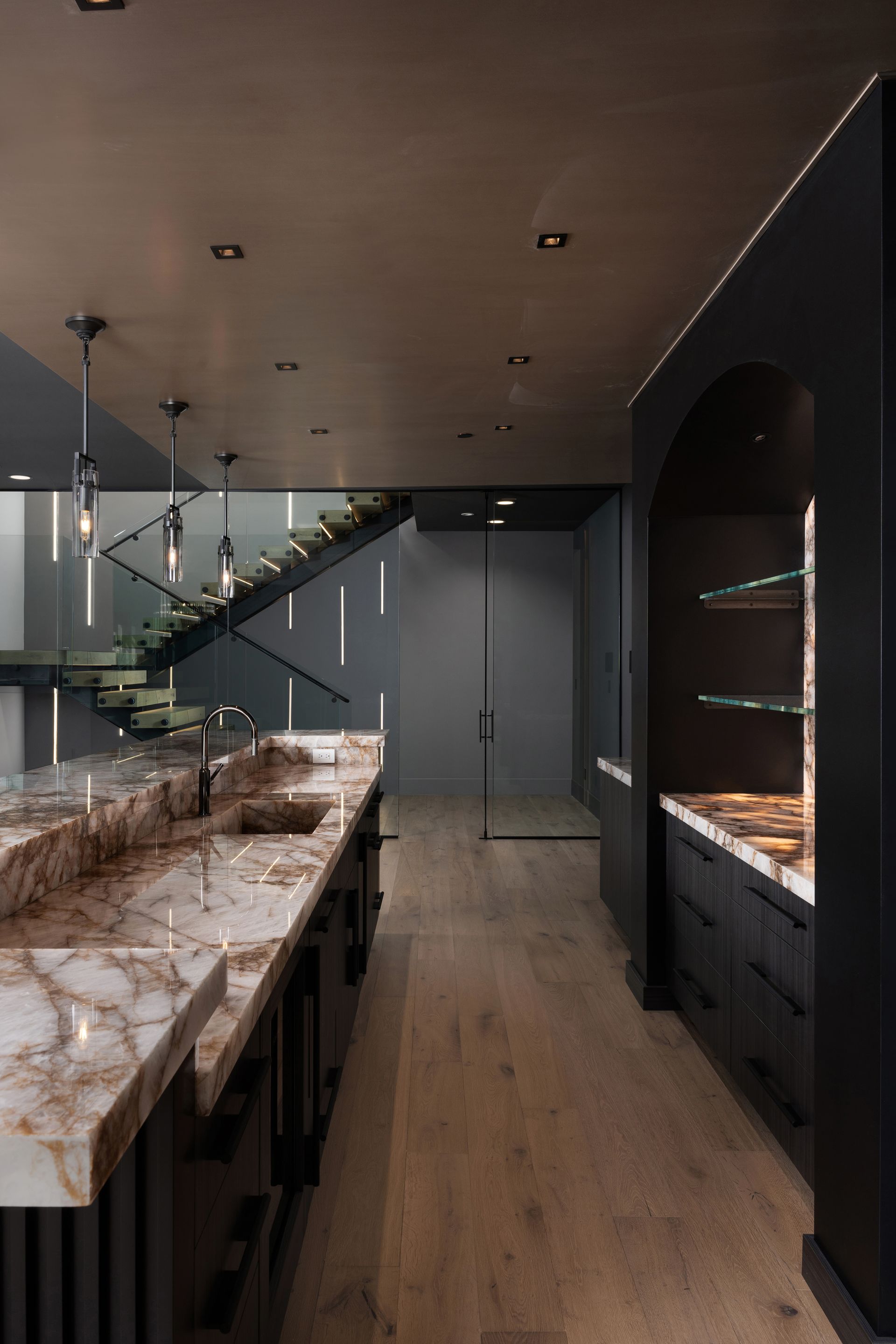 Upscale home bar with marble countertops, dark cabinets, and a staircase in the background.
