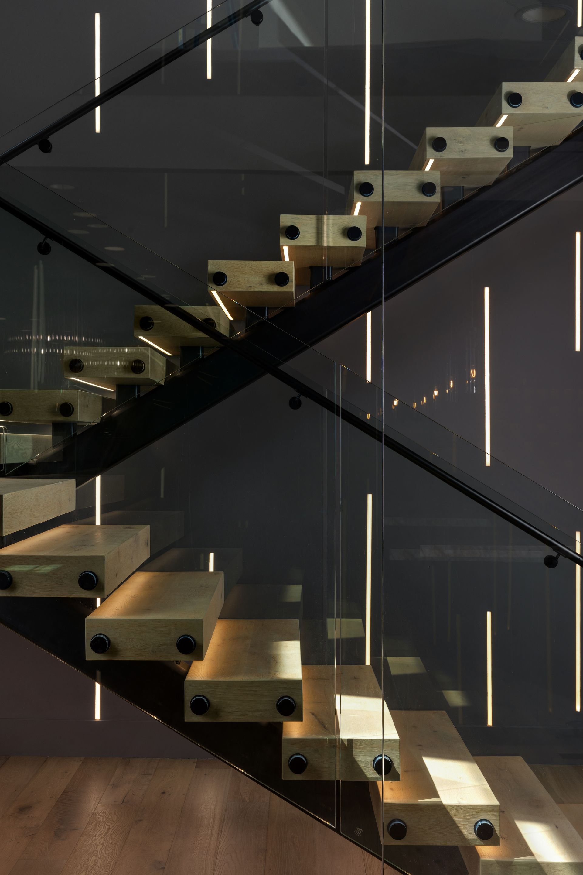 Wooden staircase with glass railing and integrated vertical lights. Dark setting.