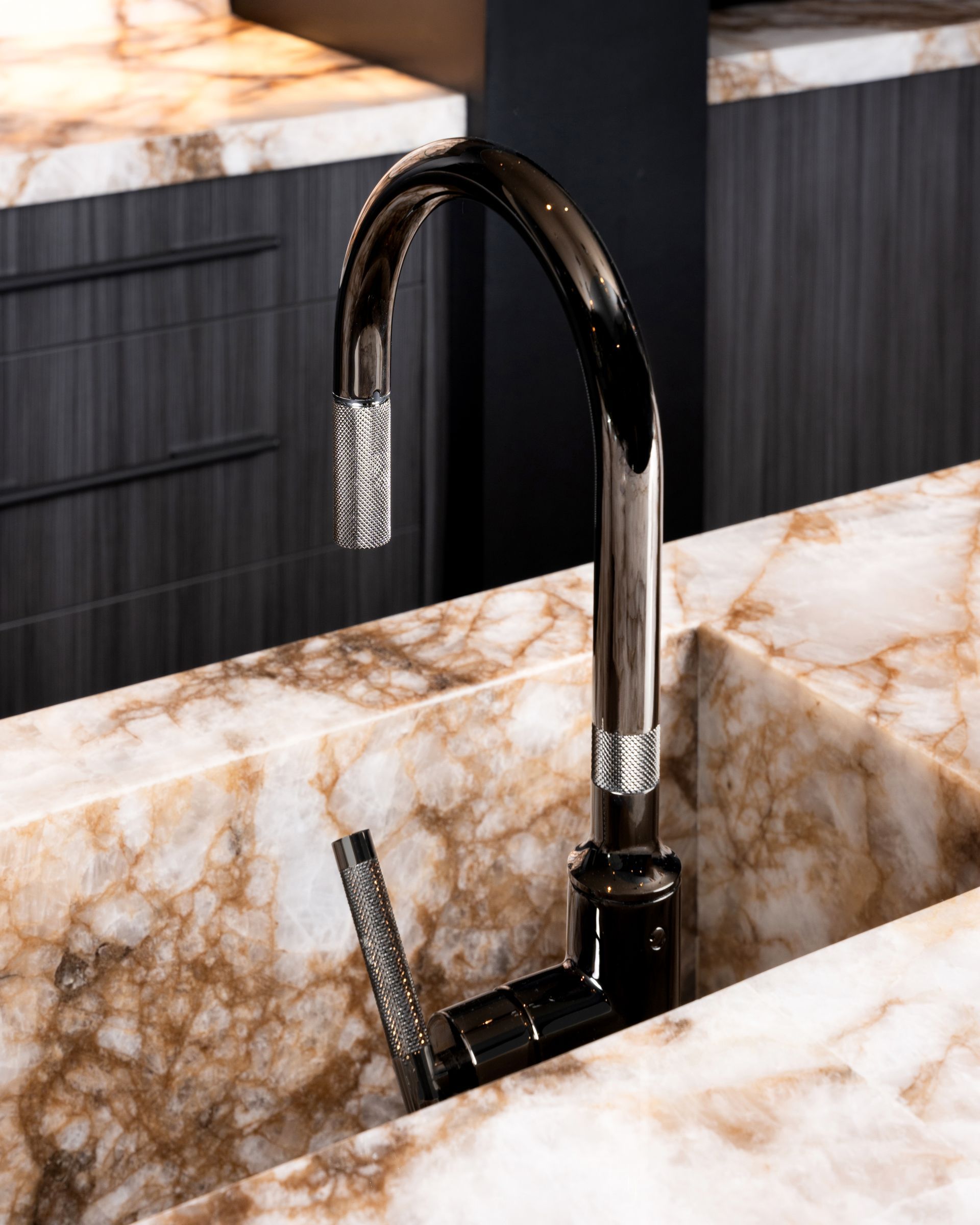 Shiny black faucet over a patterned sink. Dark cabinets in the background.