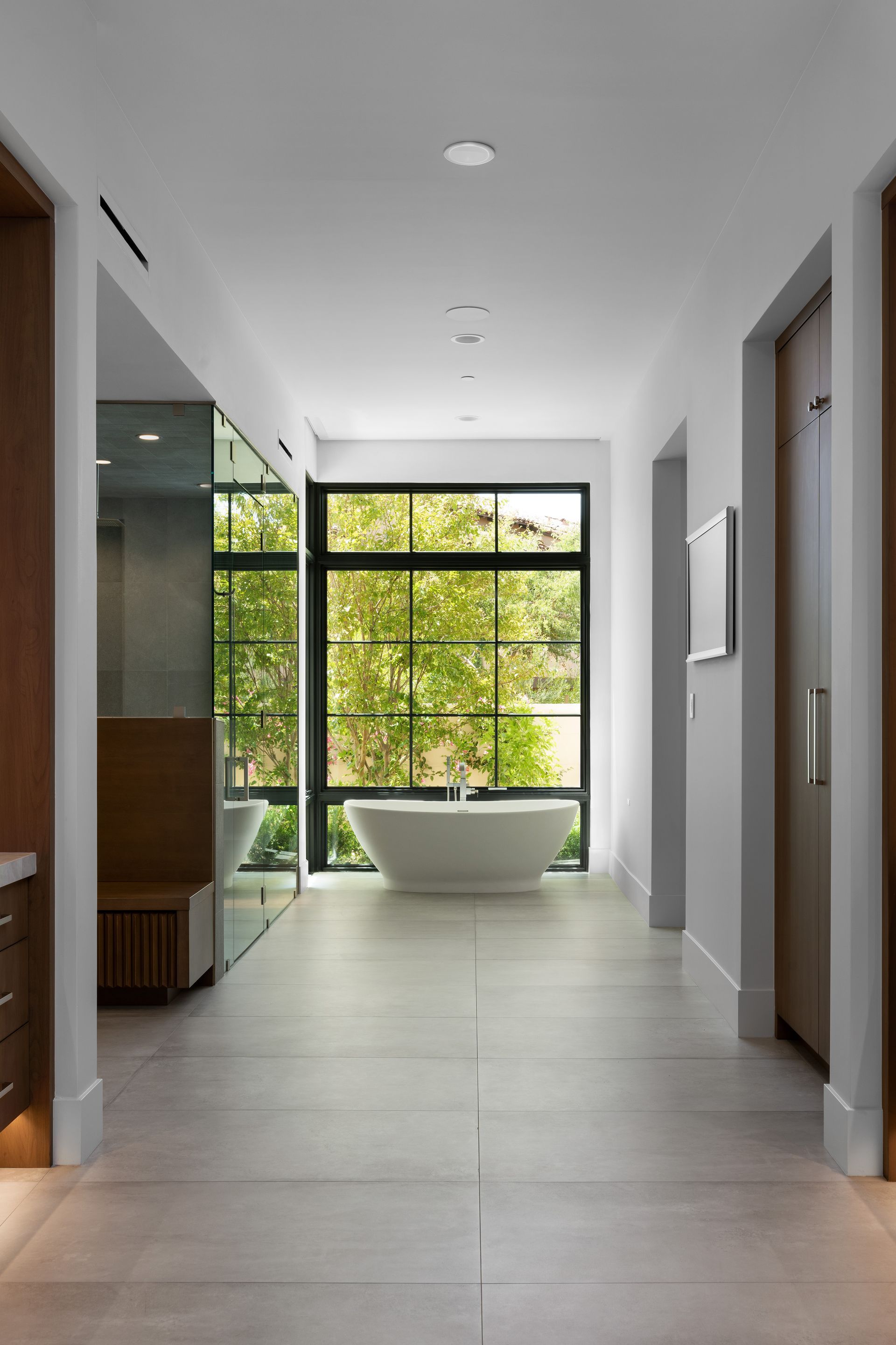 Bathroom hallway with a soaking tub in front of a window, light gray floor, and white walls.
