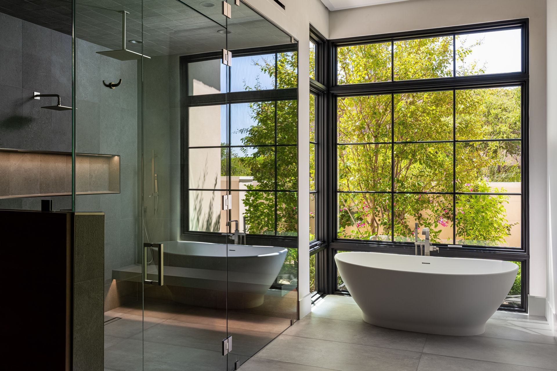 Modern bathroom with large windows, a freestanding tub, and a glass-enclosed shower.