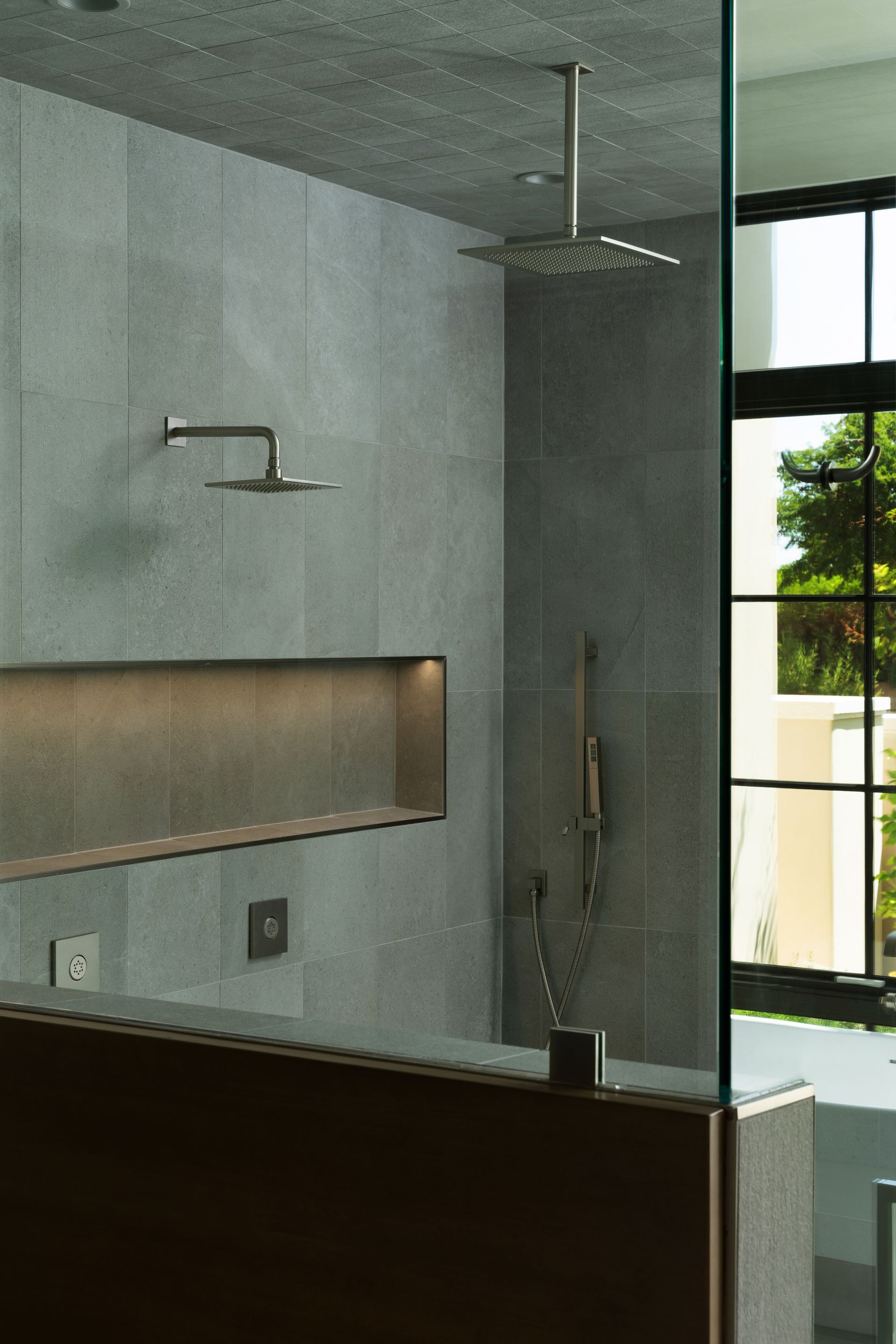 Modern bathroom with gray tile walls, glass shower door, and two showerheads.