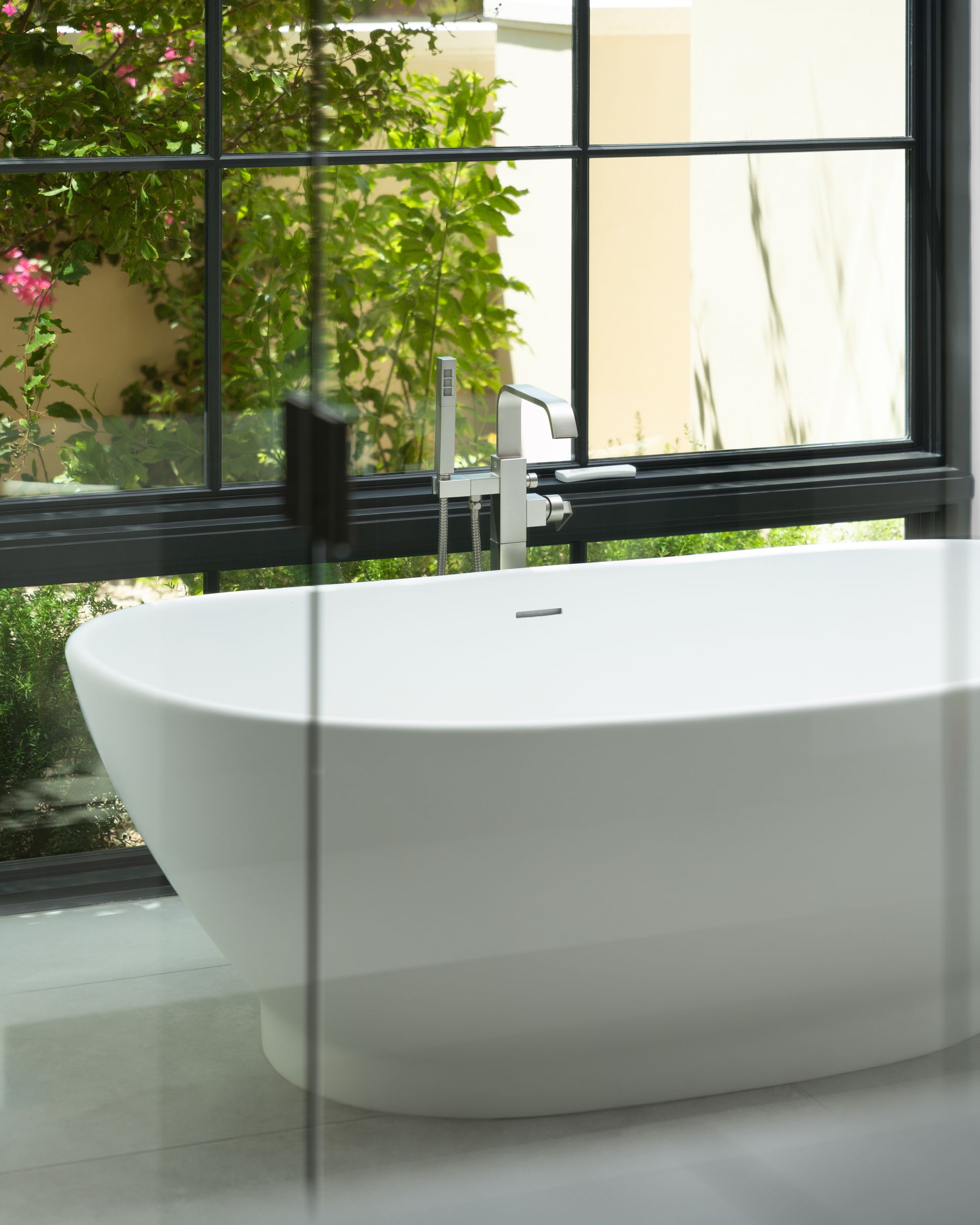 White oval bathtub with chrome faucet near a window overlooking greenery.