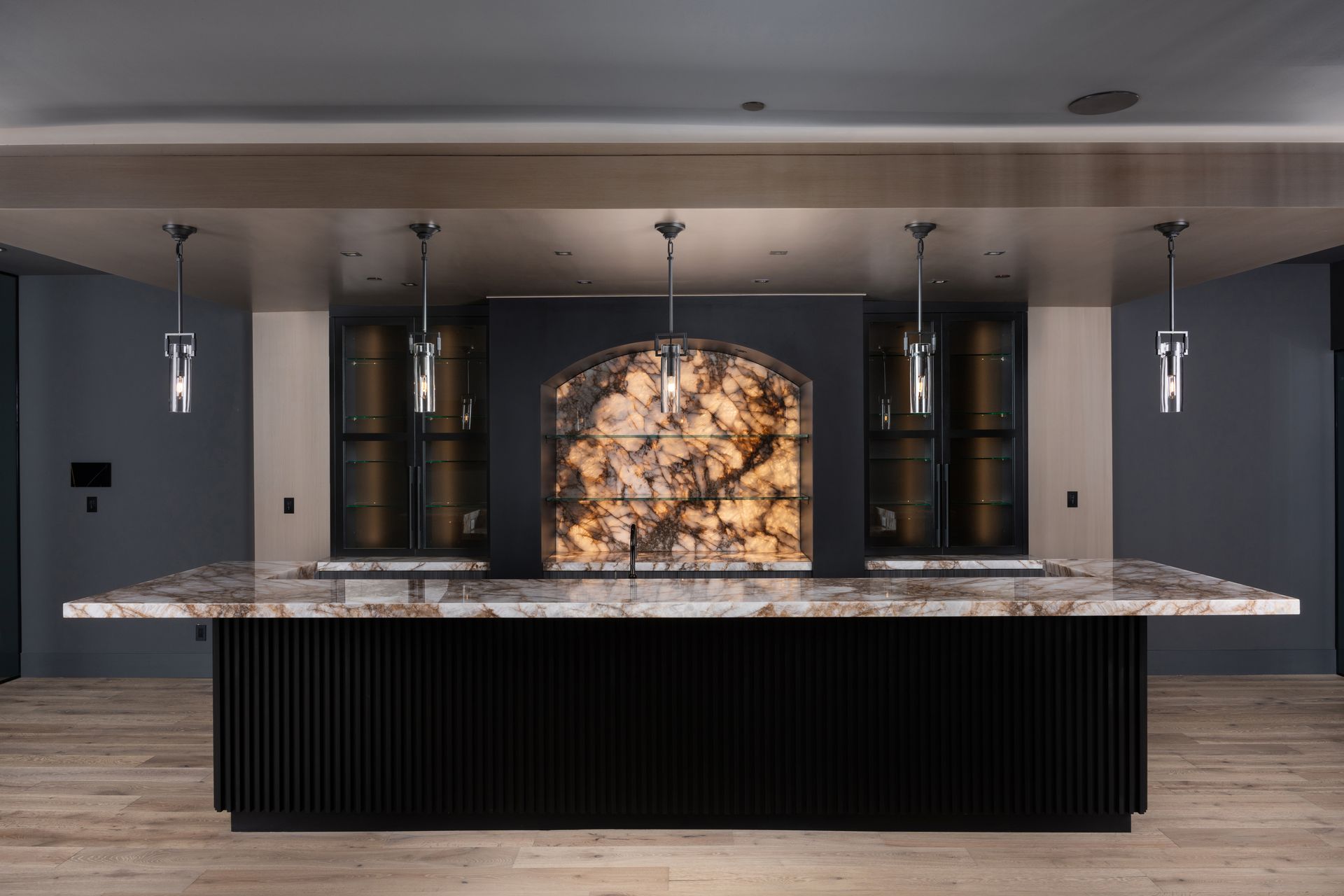 Bar with marble countertop, black base, and backlit feature, under pendant lights.