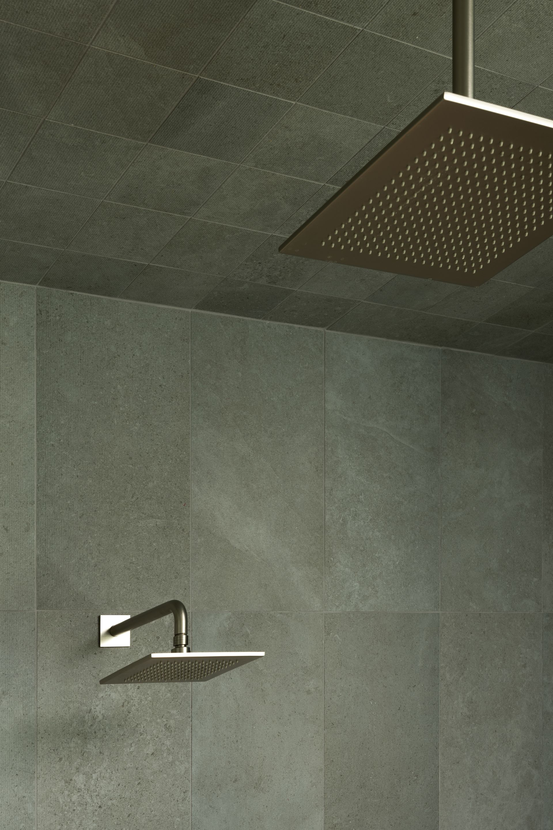 Square shower heads on a gray tiled wall and ceiling. One head is overhead, the other mounted on wall.