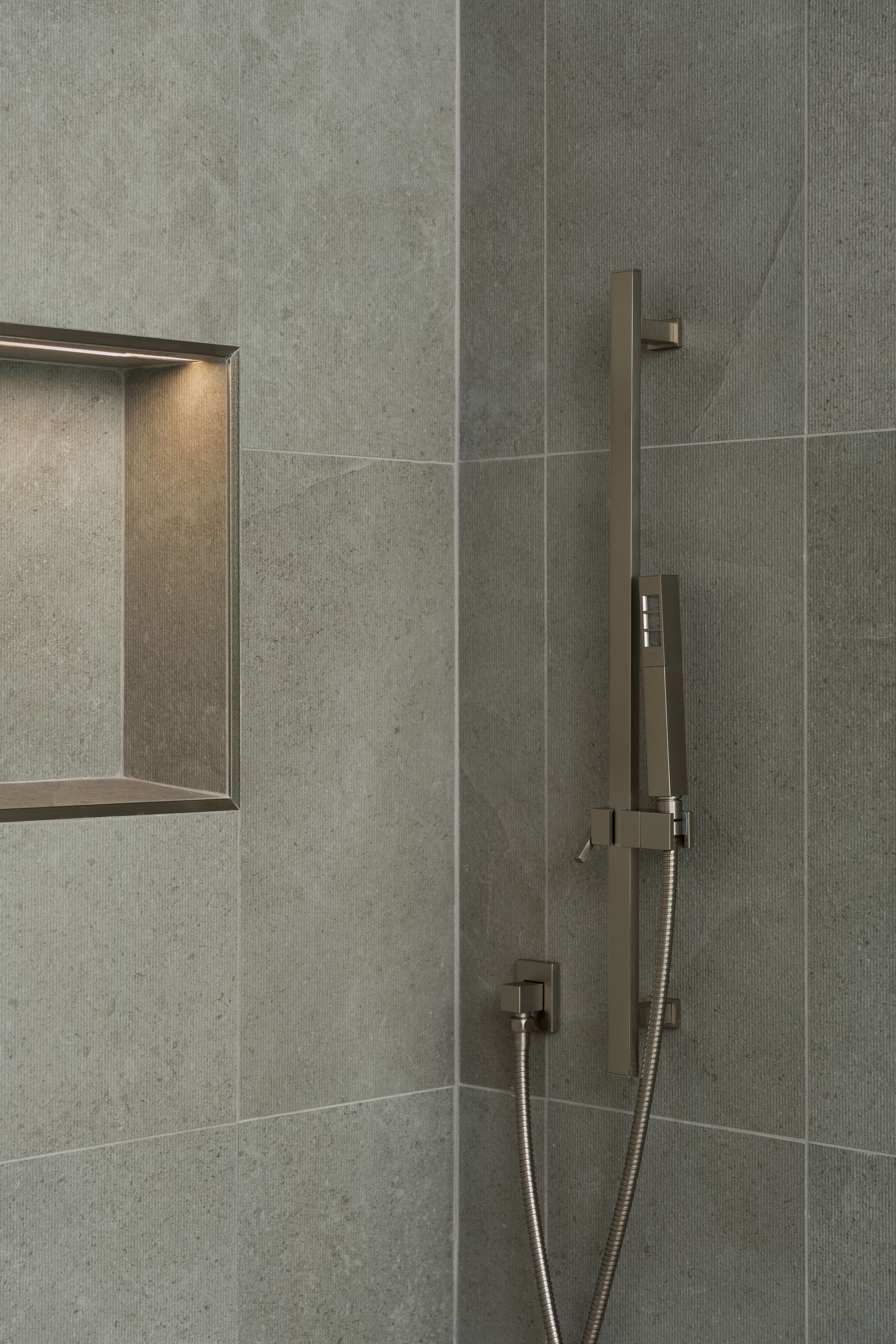Gray tiled shower with recessed shelf and silver shower fixture.