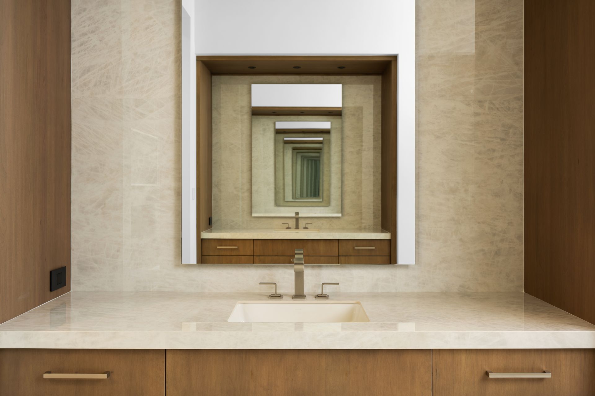 Bathroom with beige countertop, wooden cabinets and framed mirror, creating an infinite reflection.