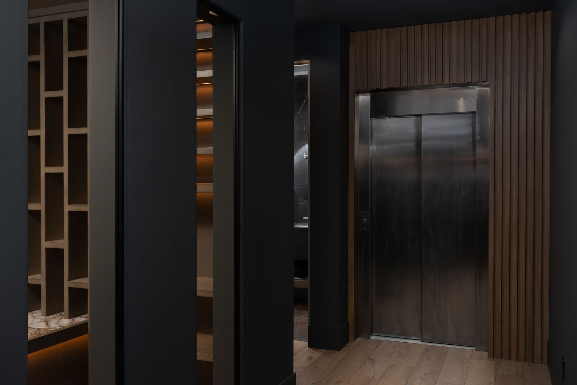 Dark hallway with a stainless steel elevator, wooden accent walls, and a built-in shelving unit.