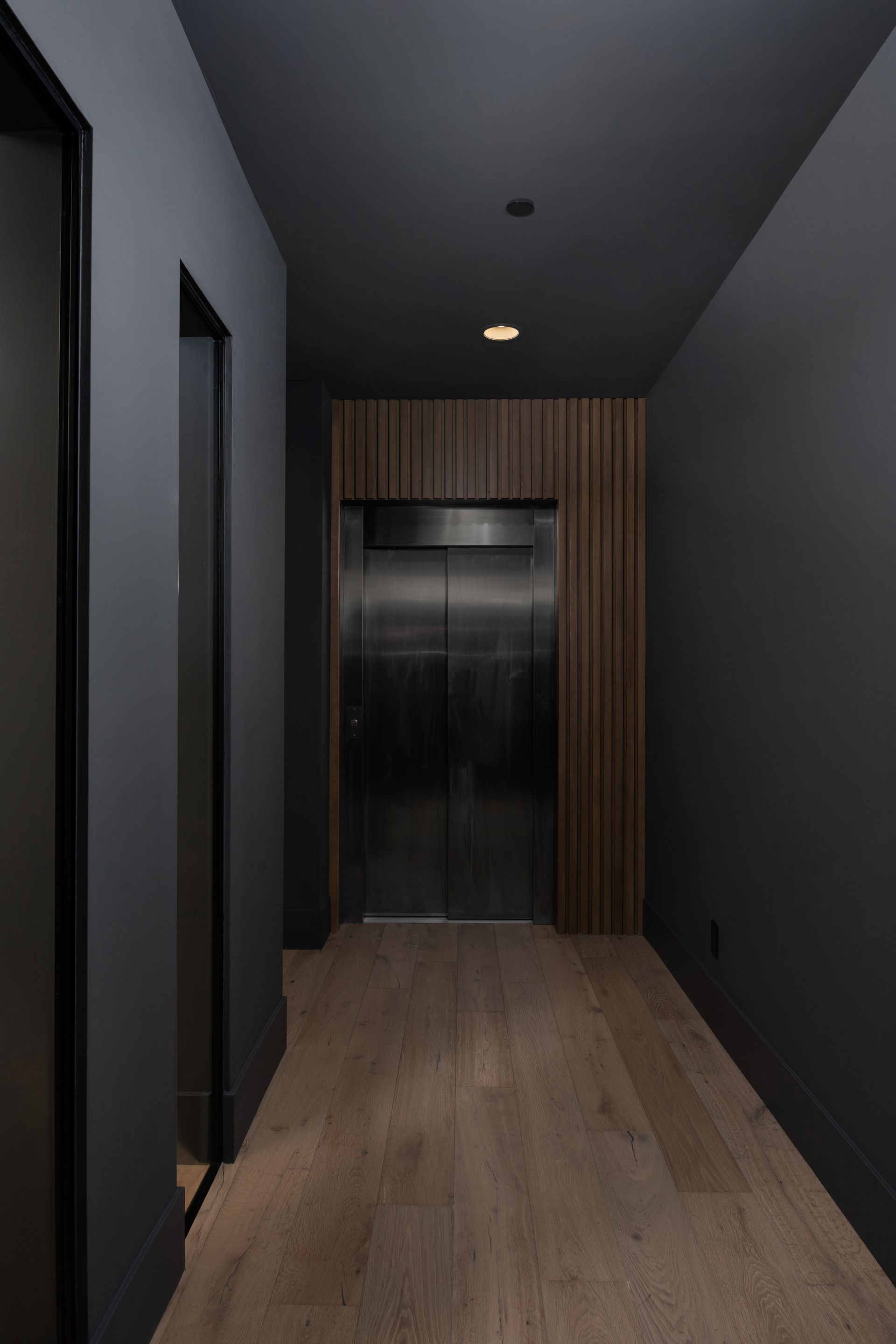 Hallway with a dark gray color scheme, a wooden floor, and an elevator.