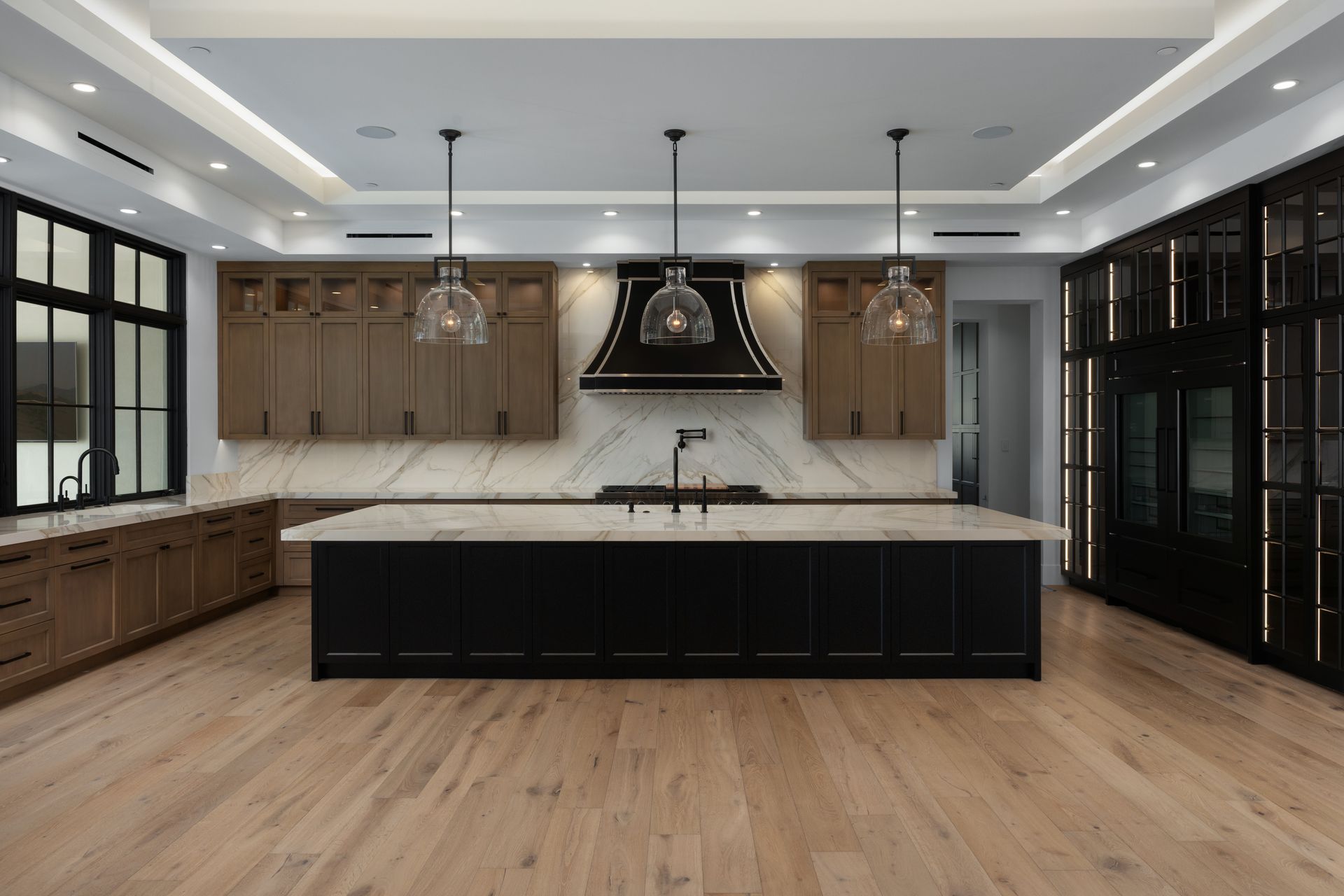 Modern Luxury kitchen with light wood floors, dark island, marble countertops, and black cabinetry.