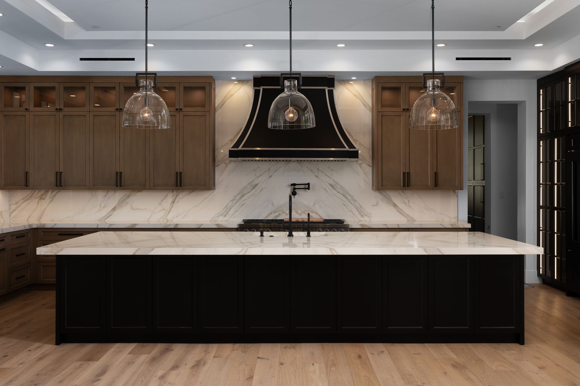 Luxury Modern Kitchen with black marble island, wooden cabinets, marble backsplash, and hanging lights.