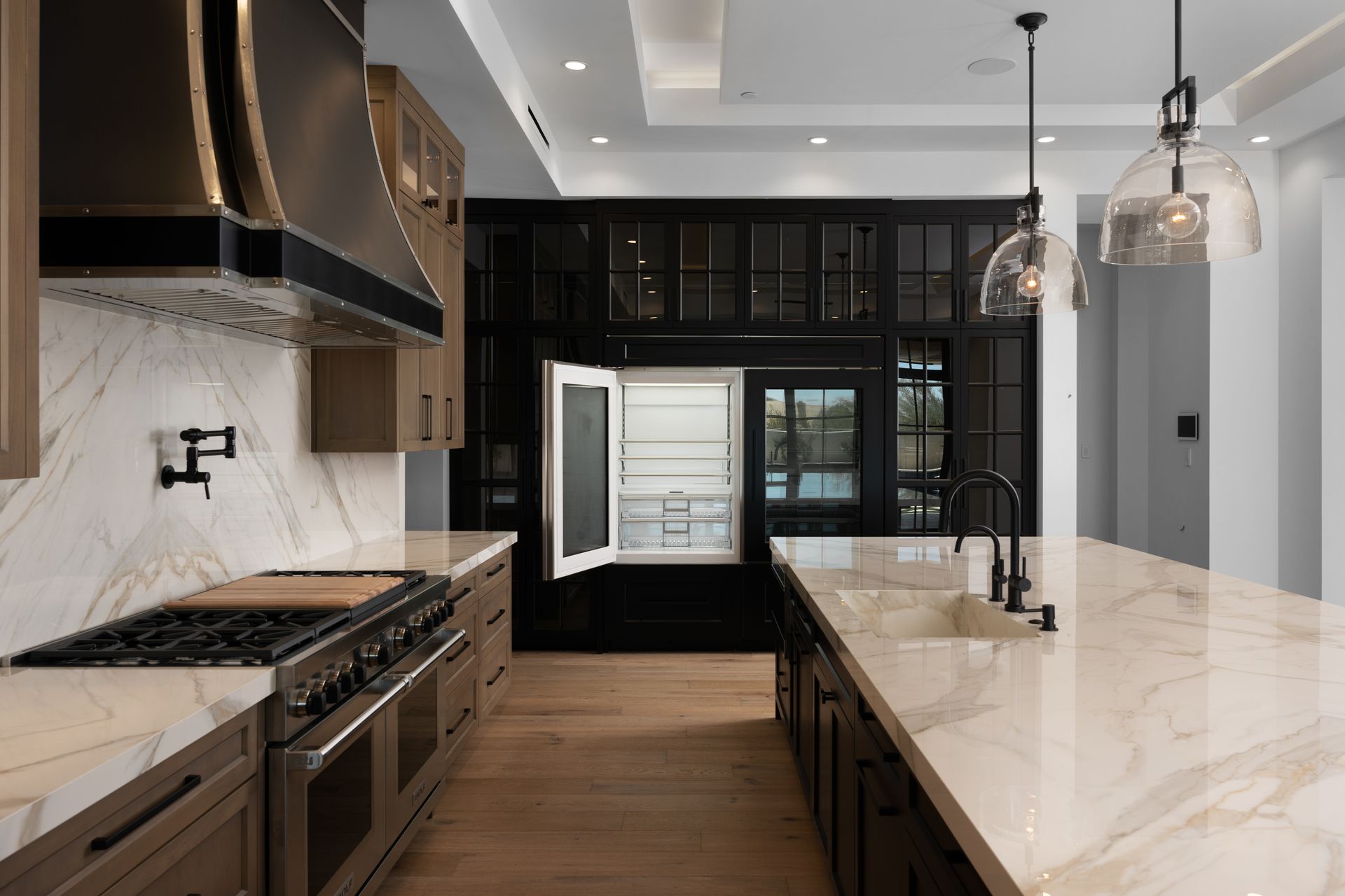 Modern kitchen with marble countertops, wood cabinets, and black accents; a refrigerator is open.