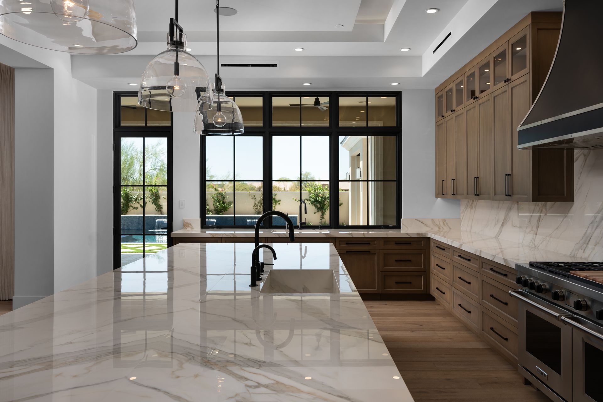 Modern kitchen with marble countertops, wood cabinets, and large windows.