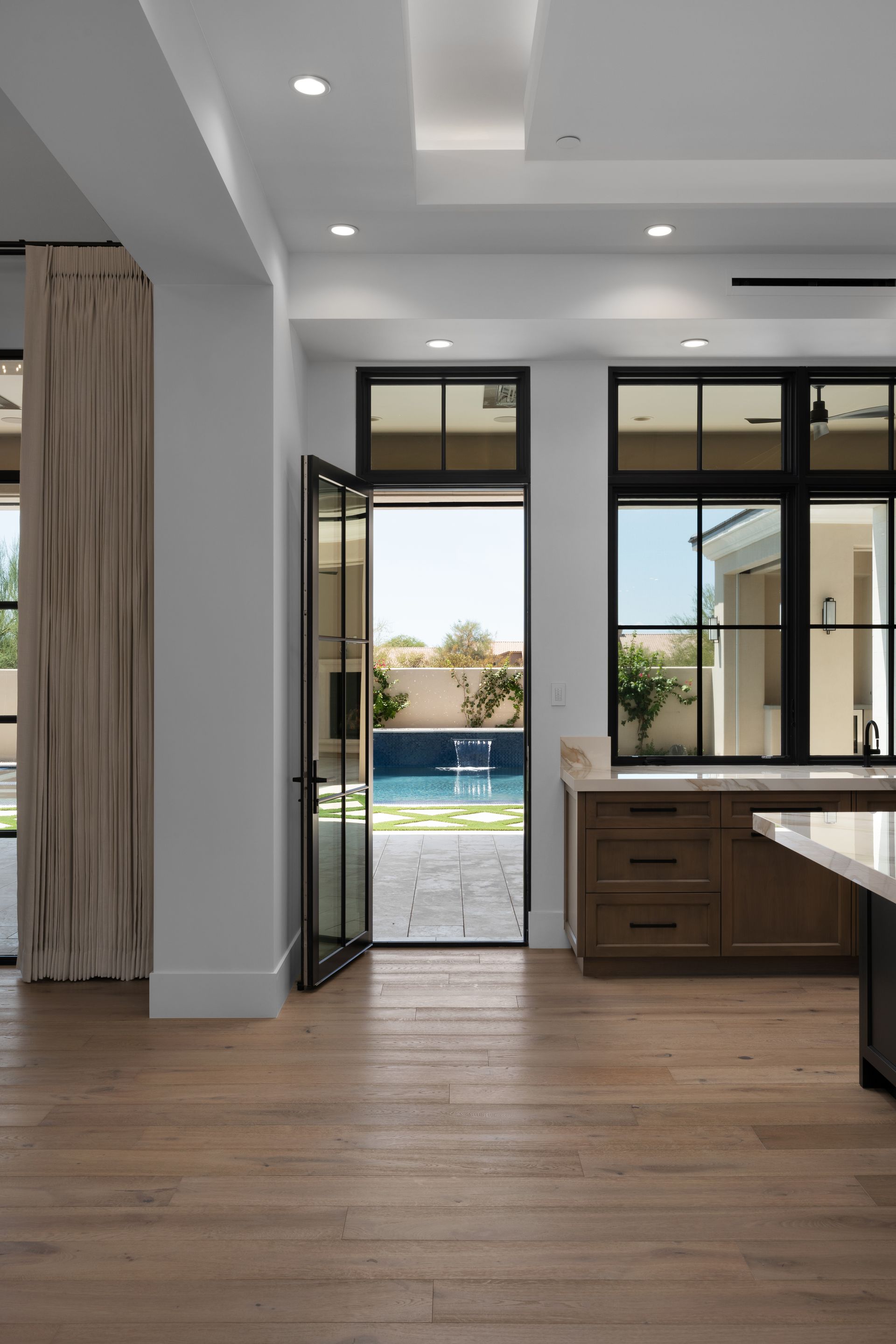 Interior view: kitchen with wooden cabinets, French doors opening to a pool area; hardwood floors.