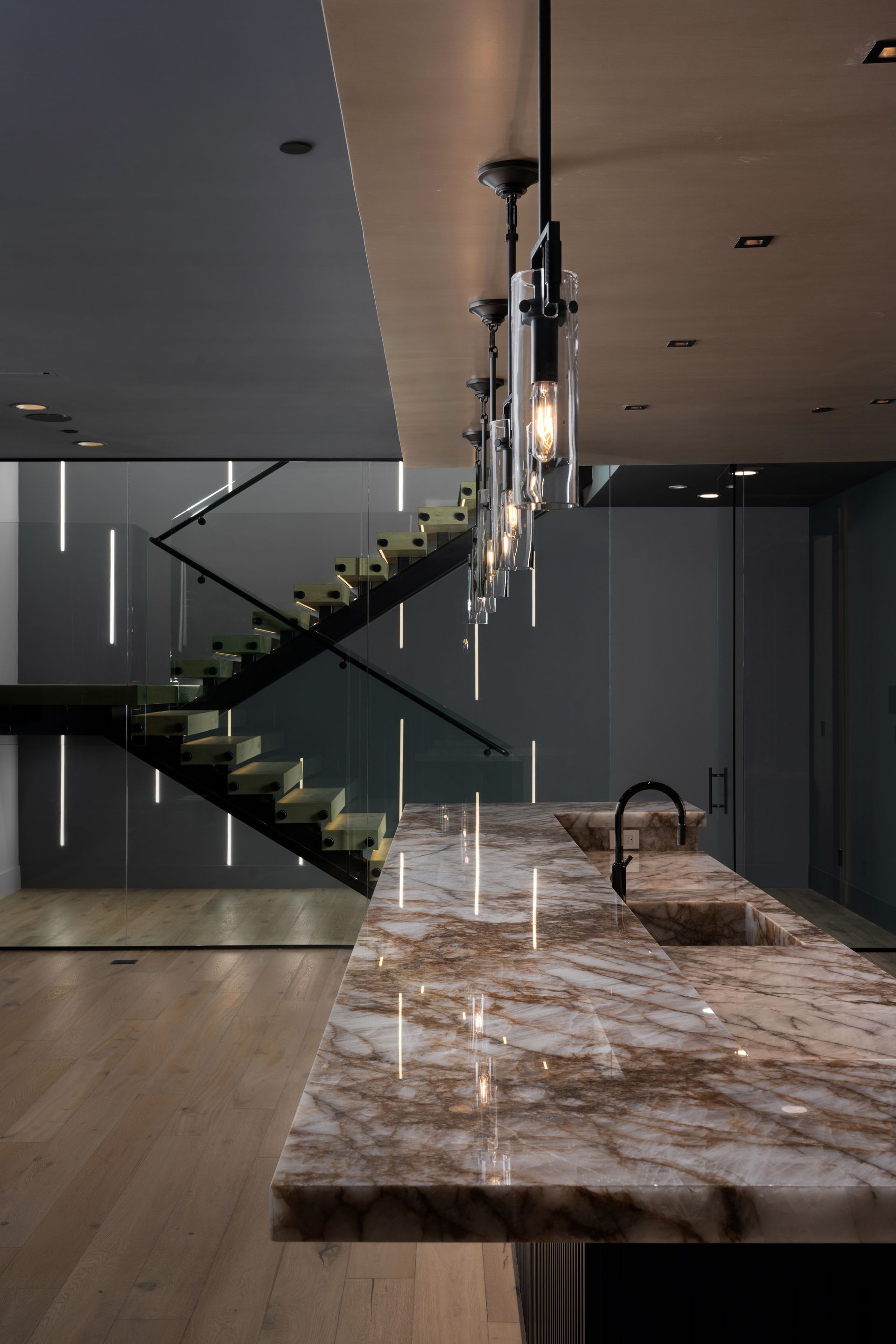Modern kitchen with marble island, black fixtures, and a staircase with vertical lighting.