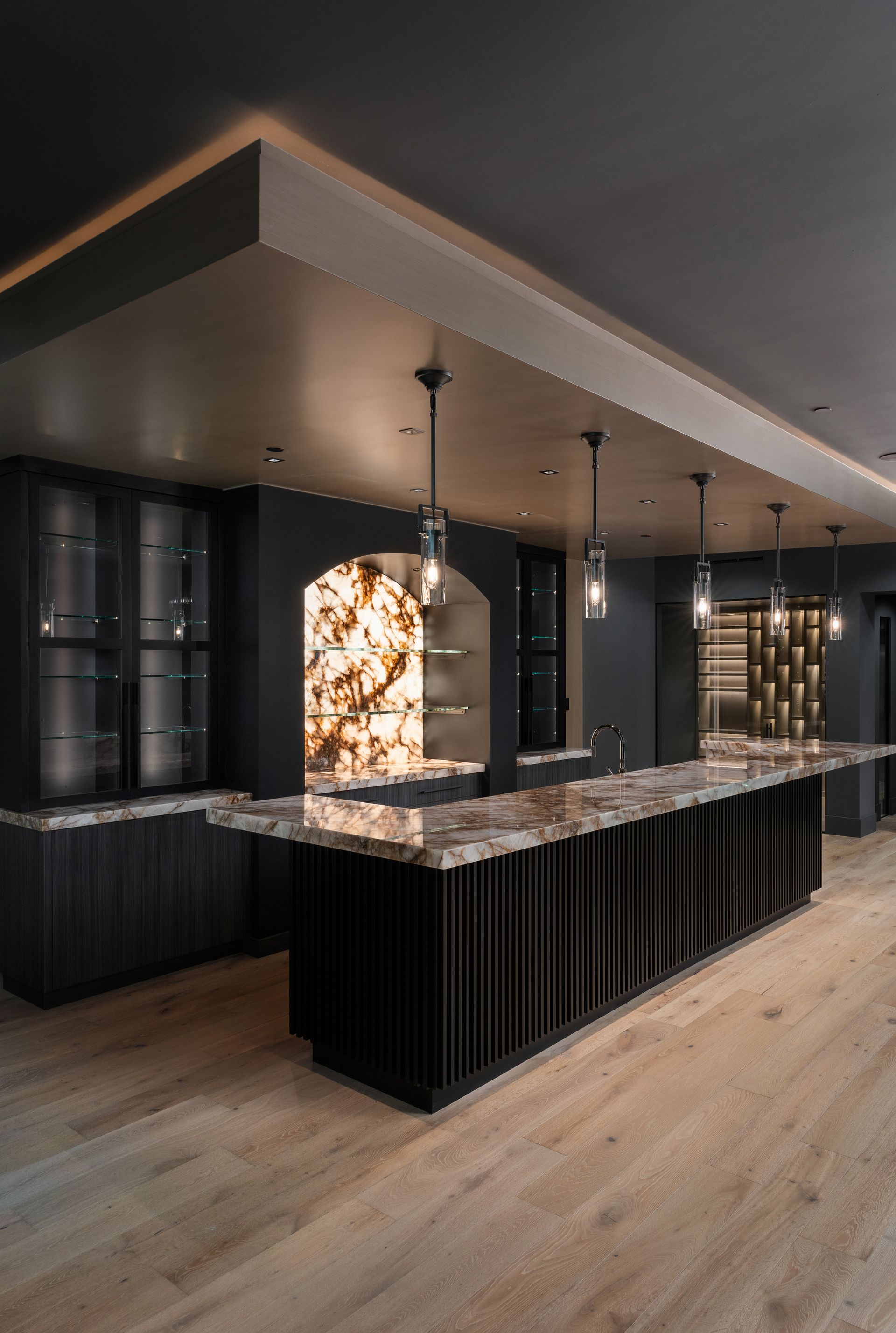 Dark modern bar with onyx accent, black cabinets, pendant lights, and light wood flooring.