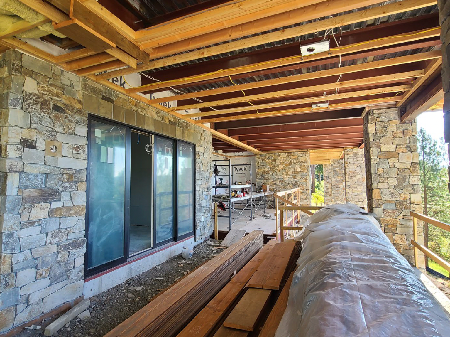 Exterior of a building under construction, featuring stone walls, wooden beams, sliding doors, and lumber.