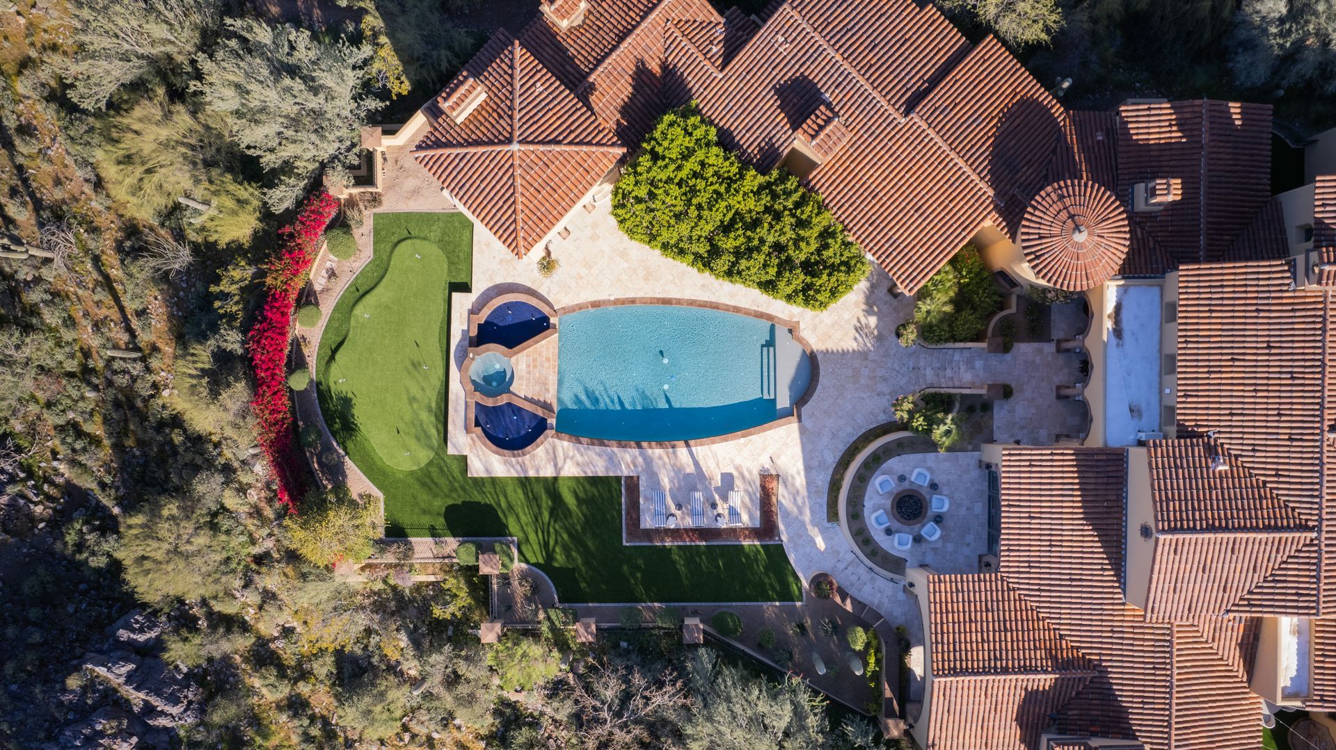 Overhead view of a luxury house with a swimming pool, lawn, and surrounding trees.