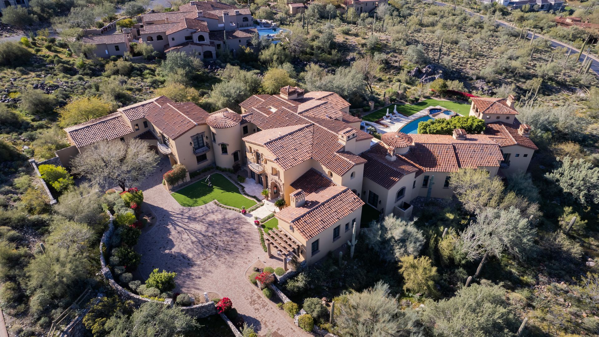Aerial view of a large, multi-sectioned house with a red-tiled roof surrounded by trees and a pool.