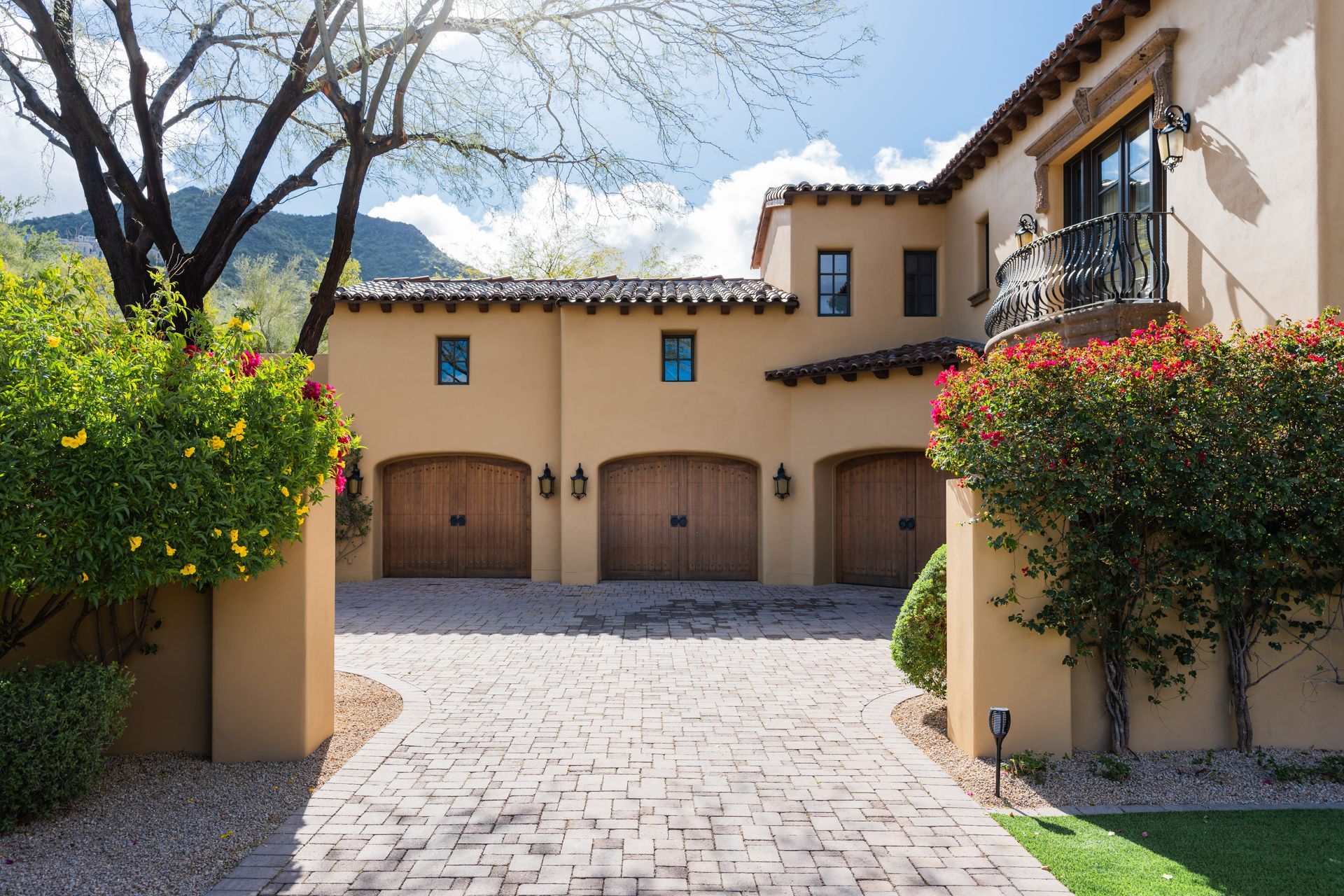 Tan stucco house with three wooden garage doors and a brick driveway.