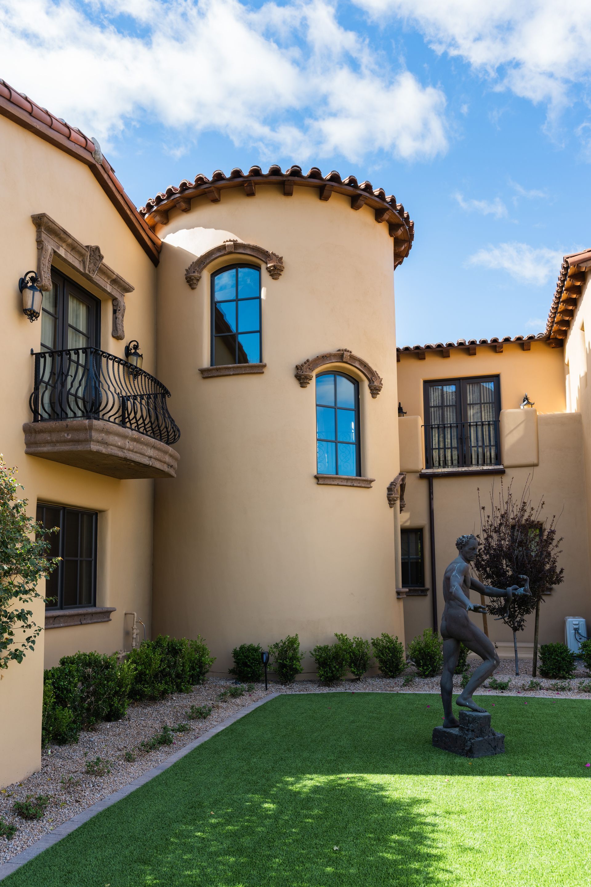 Beige stucco building with a cylindrical tower, a small balcony, and a statue in the courtyard.