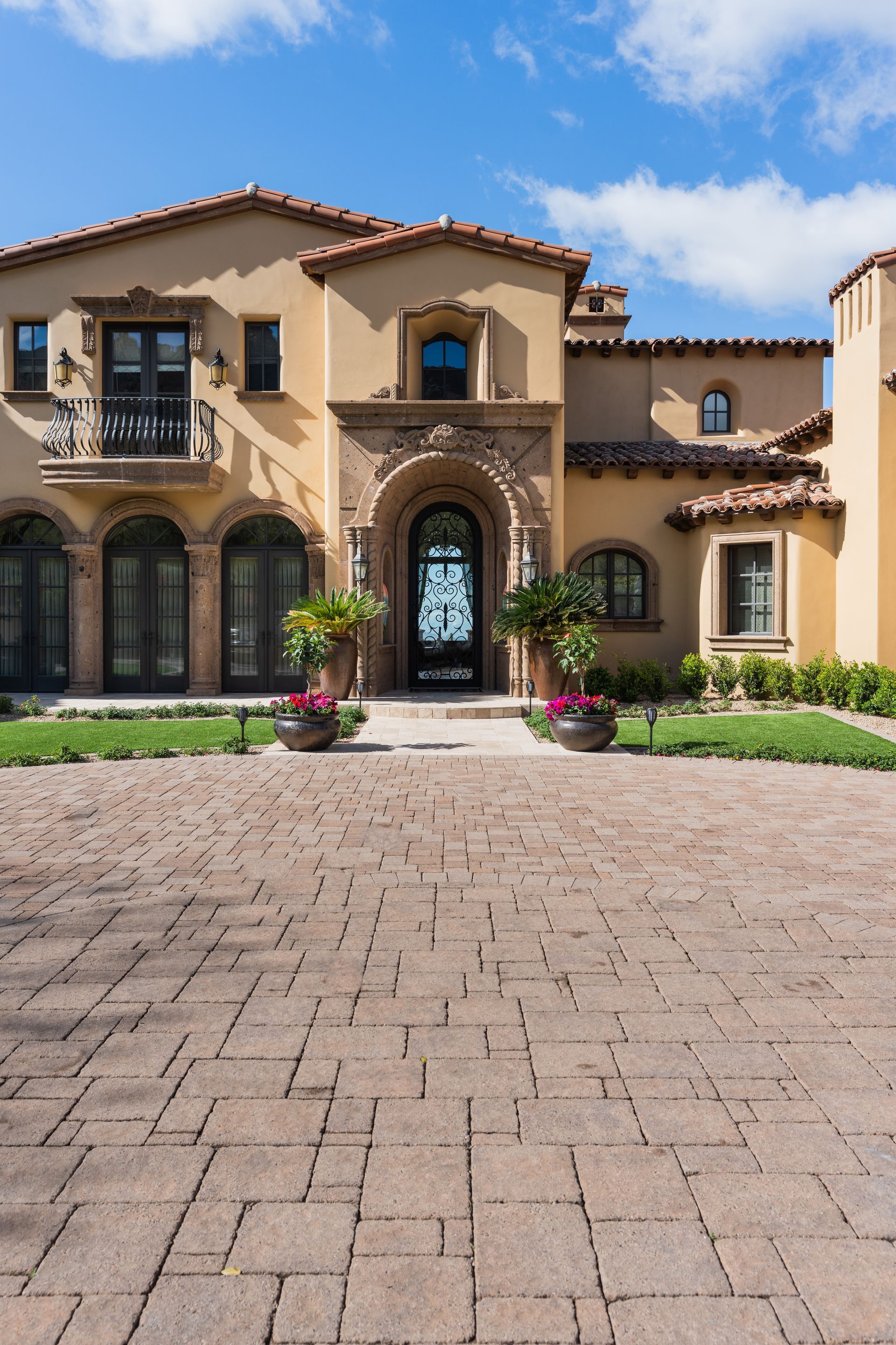Beige stucco house with arched entryway, terracotta roof, and brick driveway.